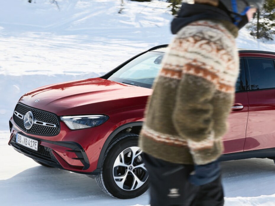 Rød Mercedes-Benz parkeret i sneklædt vinterlandskab, mens skiløber passerer