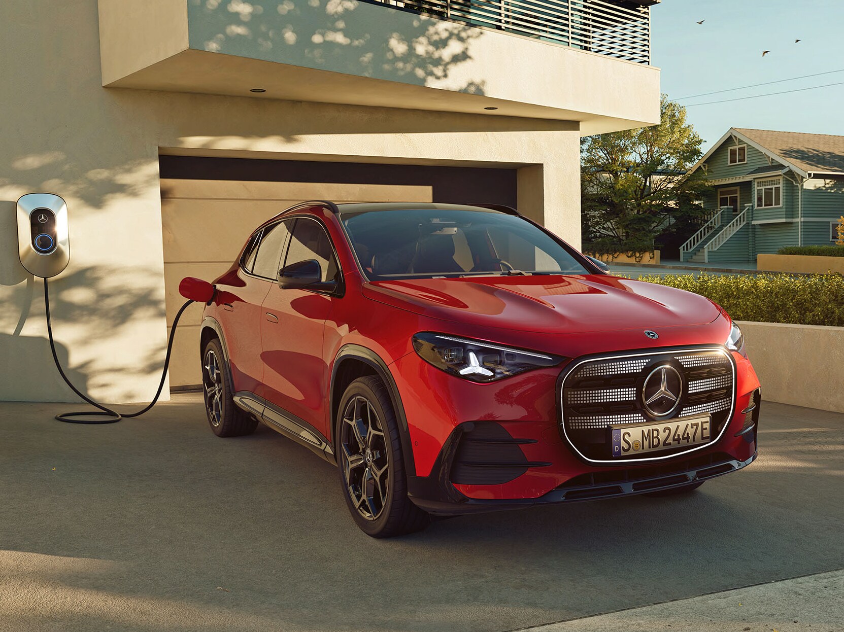 Rød elektrisk GLA fra Mercedes-Benz til opladning ved ladeboks foran et hus.