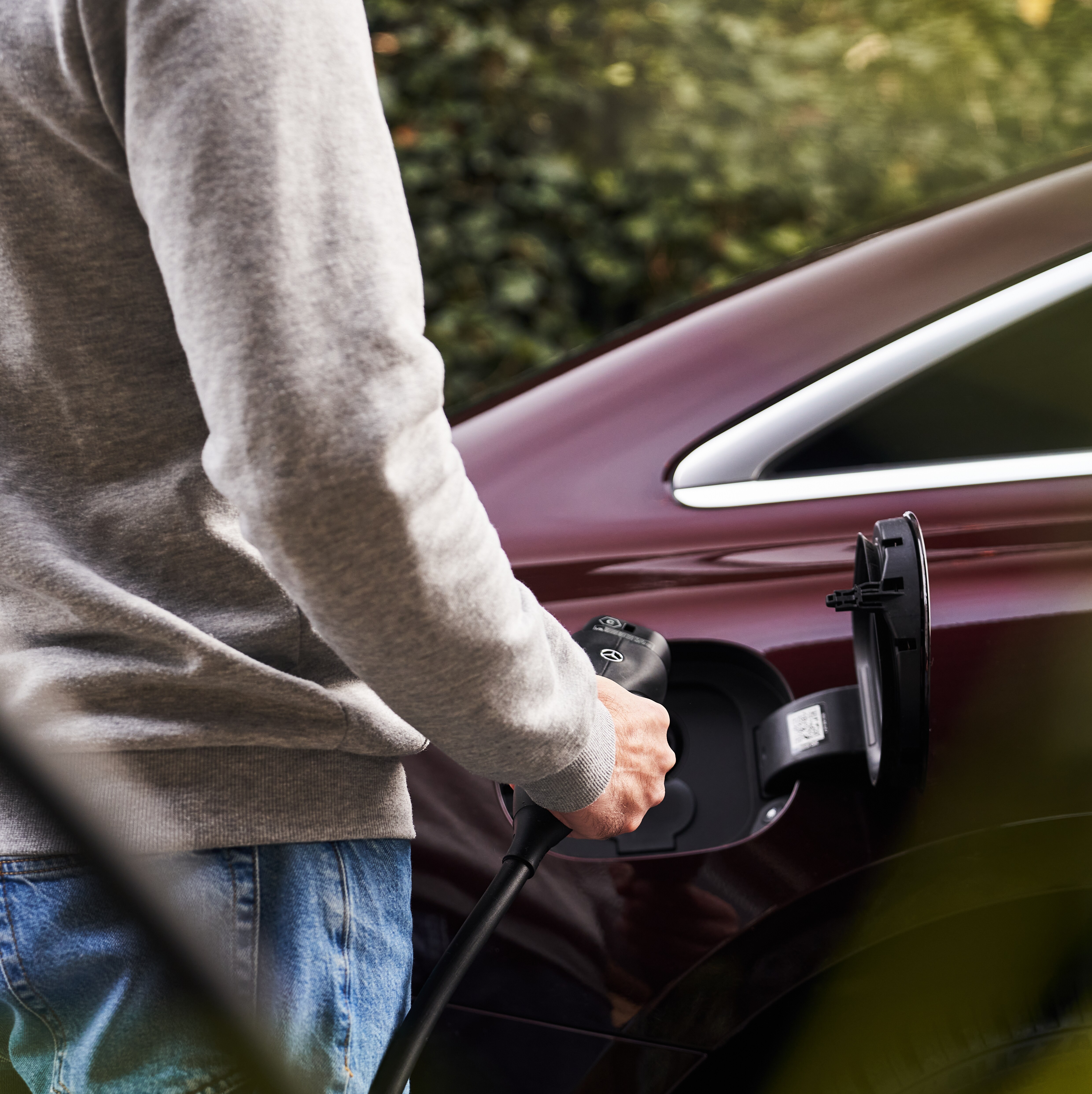 Mand sætter sin Mercedes-Benz til opladning ved en ladeboks med ladekablet i hånden.