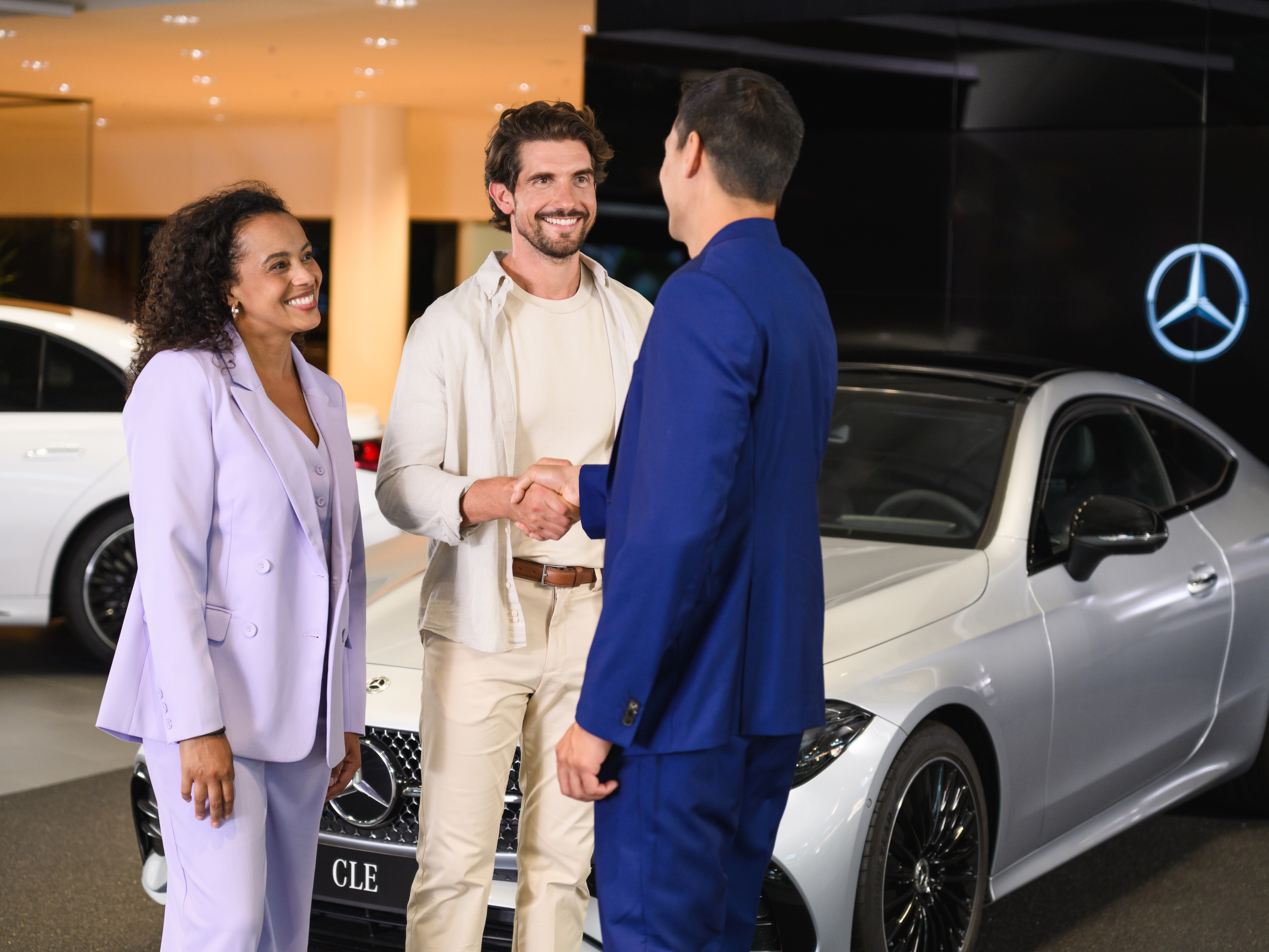 Mand og kvinde hilser på Mercedes-Benz medarbejder i et showroom.