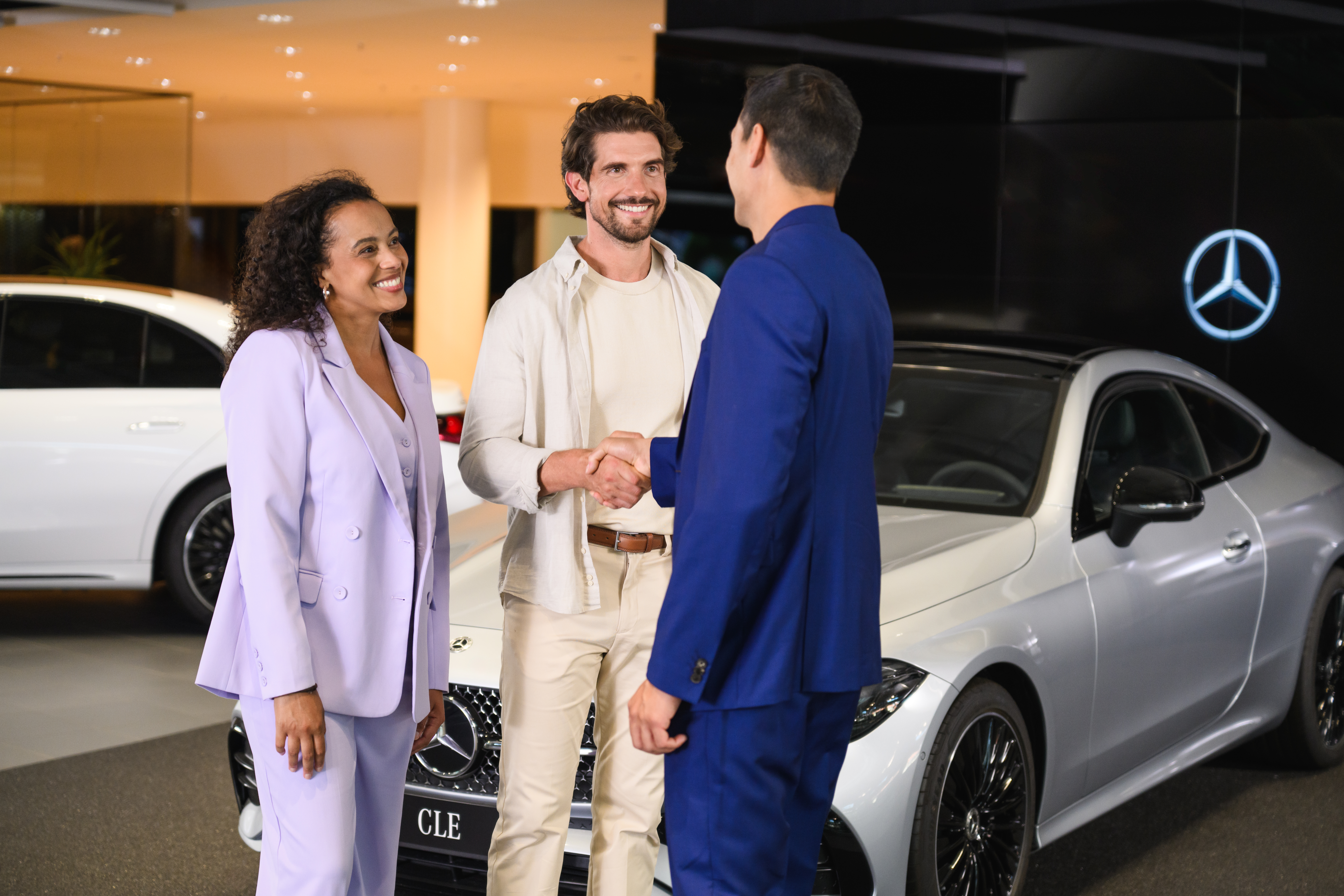 PrivatLeasing | Leasing og finansiering | Mercedes-Benz Mand og kvinde hilser på Mercedes-Benz medarbejder i et showroom.
