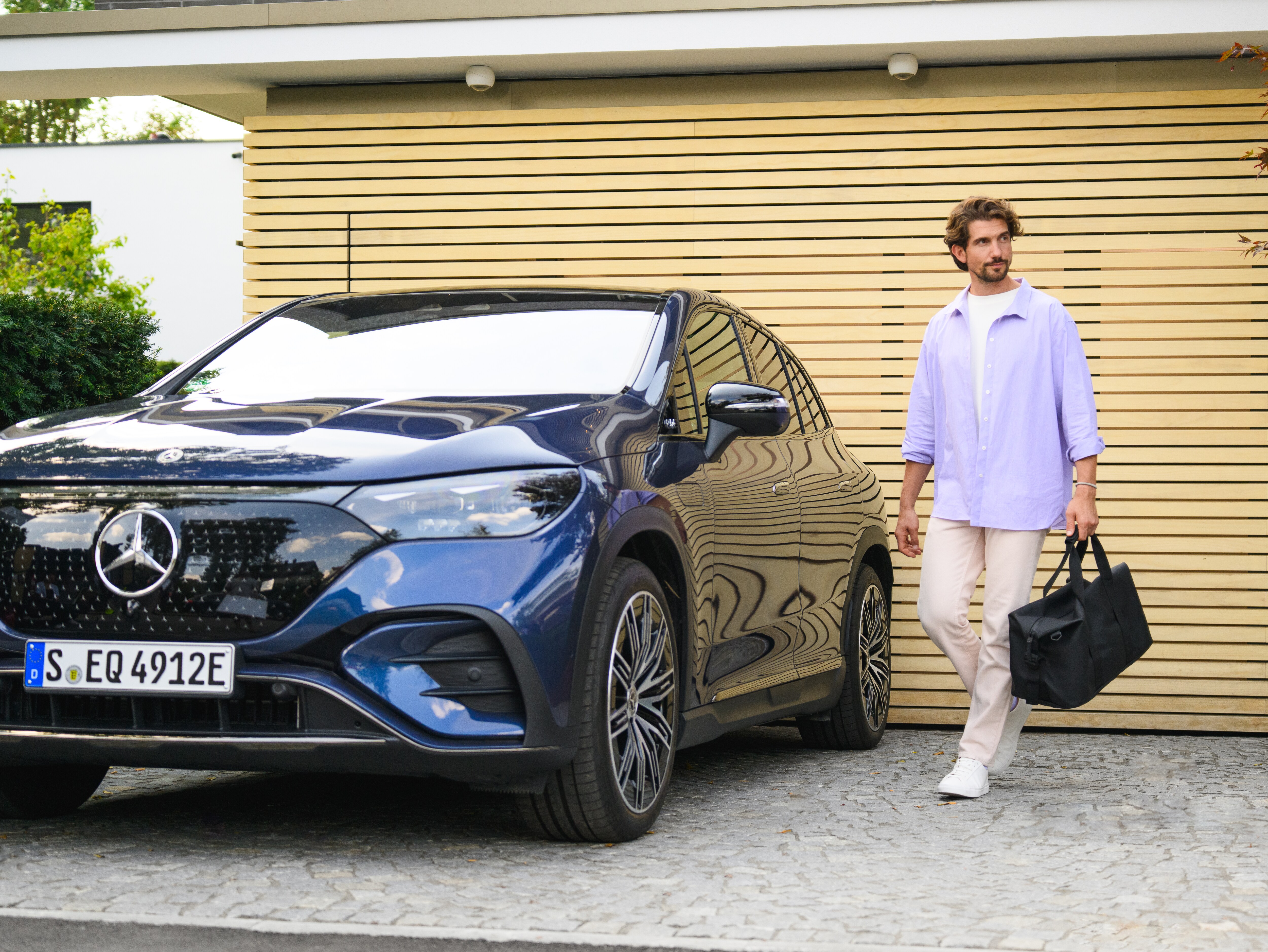 Mand går ude i sin indkørsel ved siden af en parkeret Mercedes-Benz bil.