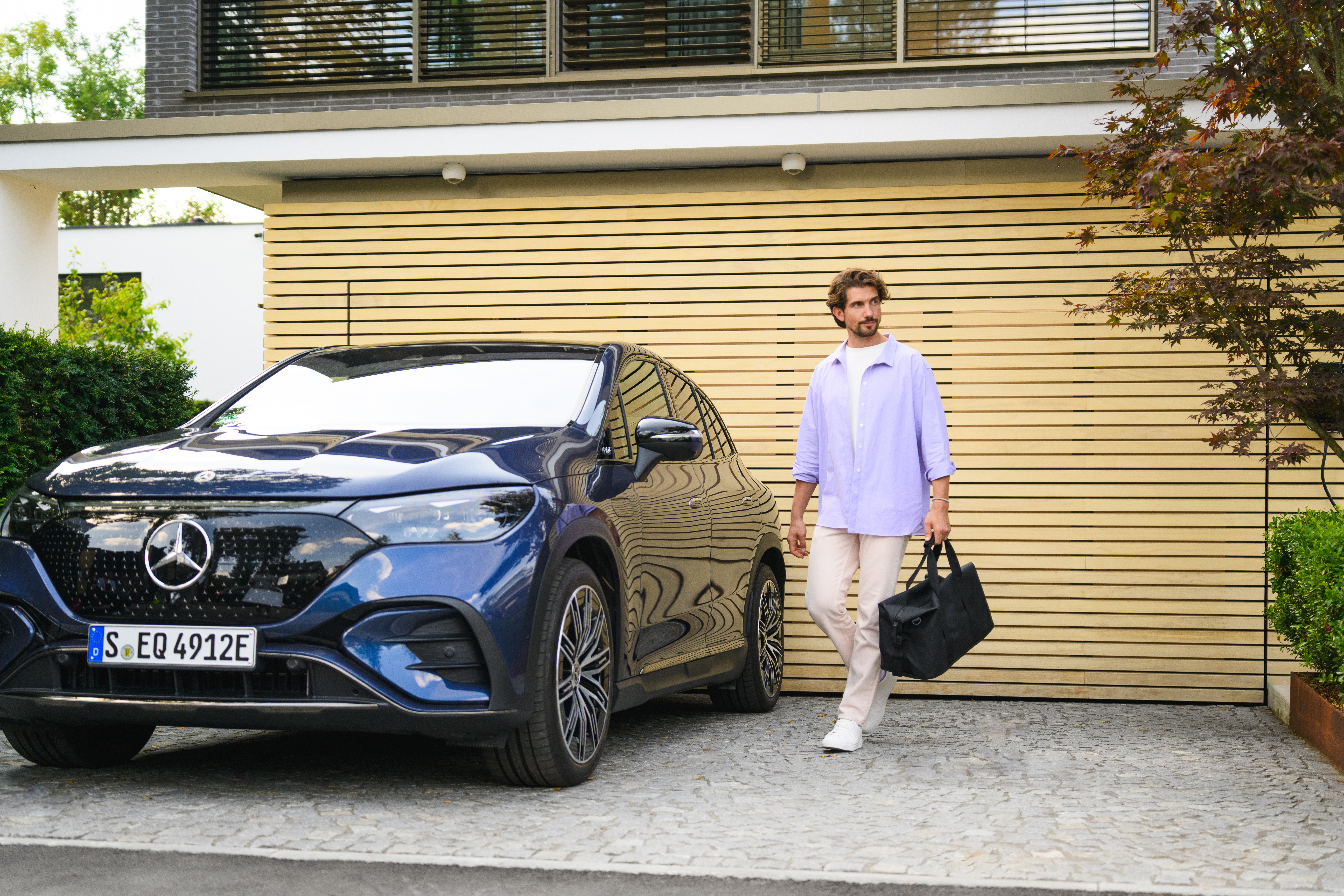 PrivatLeasing | Leasing og finansiering | Mercedes-Benz Mand går ude i sin indkørsel ved siden af en parkeret Mercedes-Benz bil.