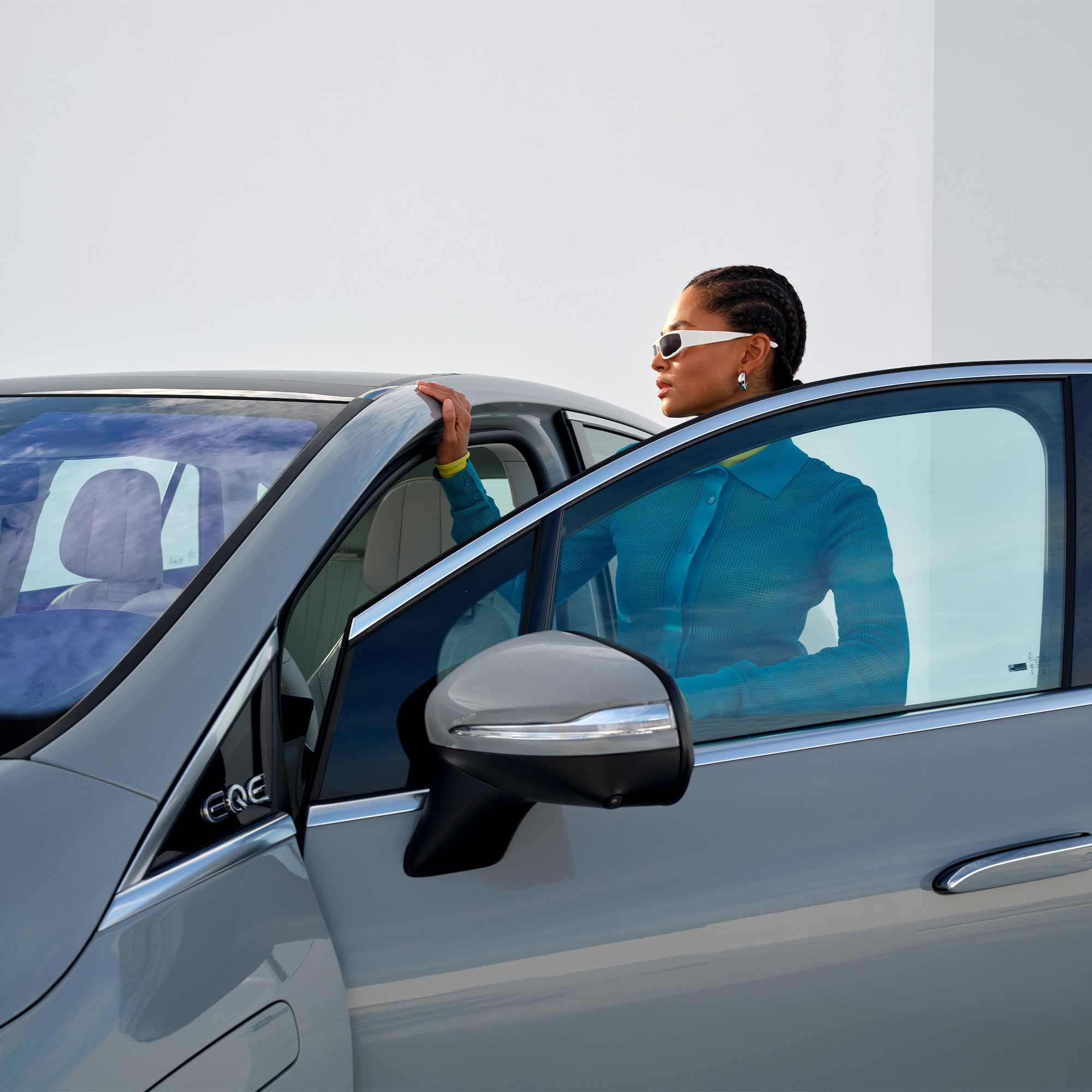 Få hele din bils historie | Servicecheck | Mercedes-Benz Kvinde med solbriller på står ved åben Mercedes-Benz EQE bildør.