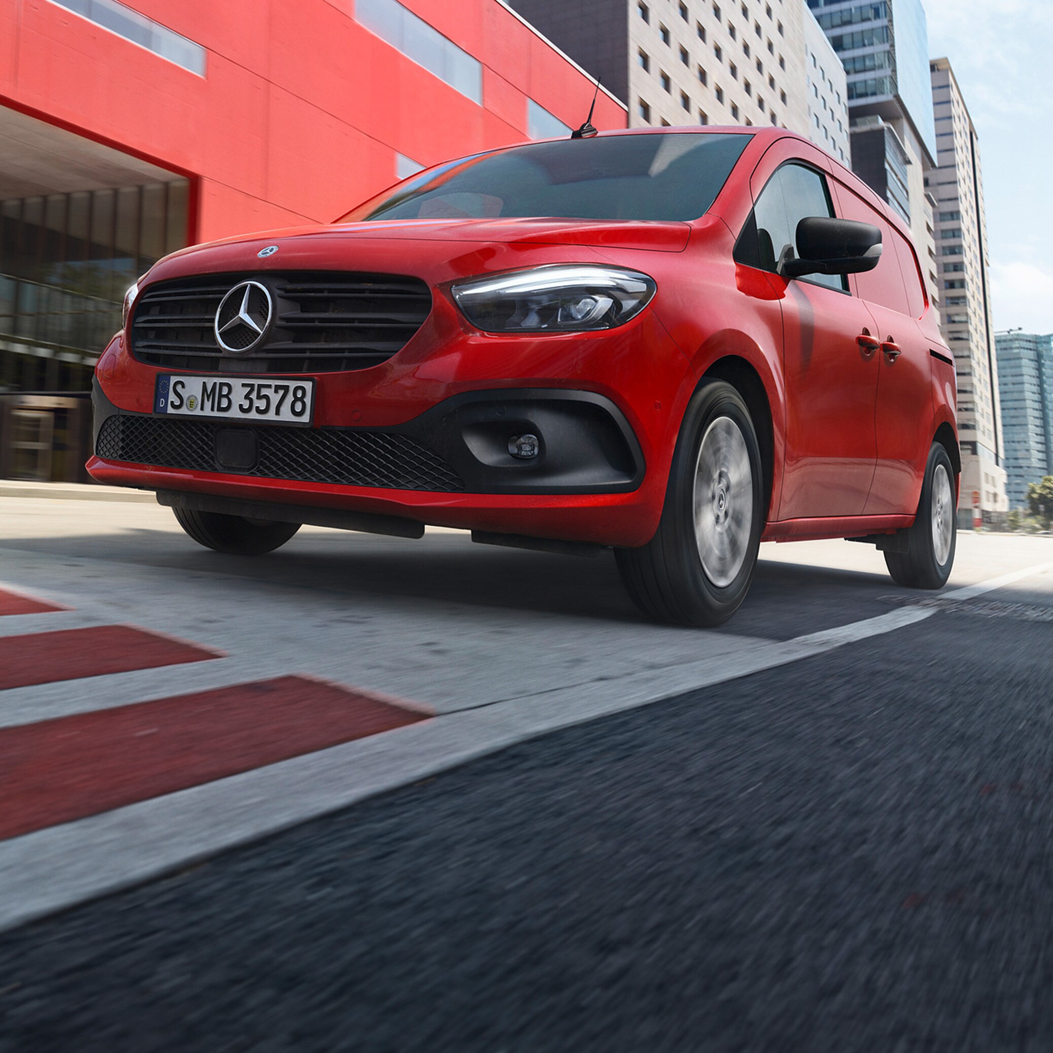 Postkasserød Mercedes-Benz eCitan på kørebanen foran rød bygning