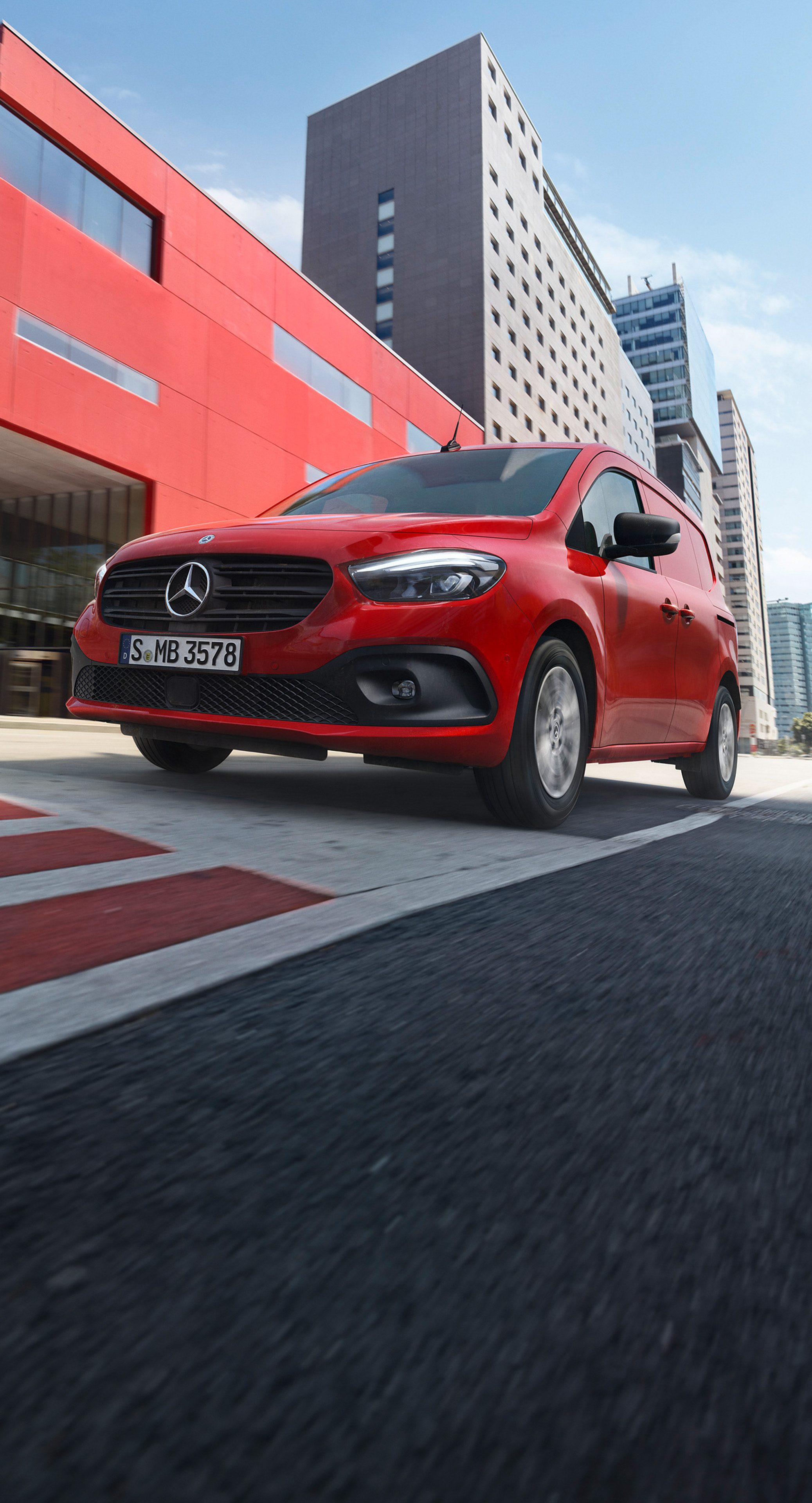 Postkasserød Mercedes-Benz eCitan på kørebanen foran rød bygning