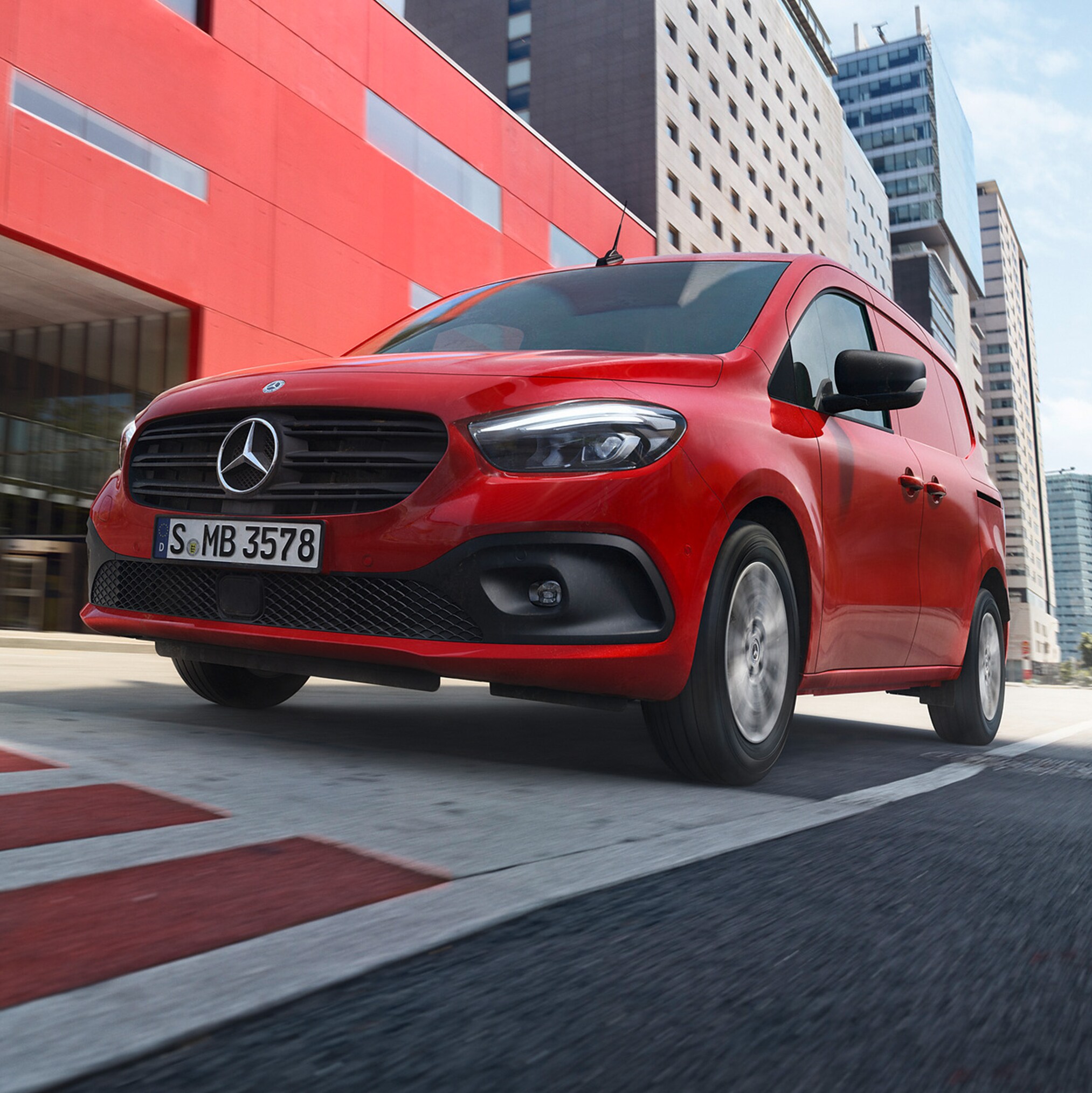 Postkasserød Mercedes-Benz eCitan på kørebanen foran rød bygning