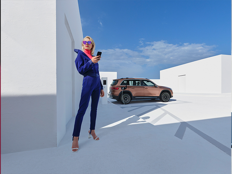 Mercedes-Benz apps | Mercedes-Benz digitale tjenester Kvinde bruger Mercedes-Benz app, mens elbil lader i baggrunden