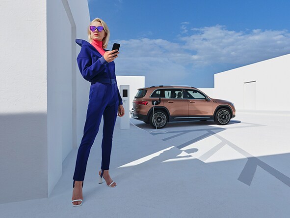 Kvinde bruger Mercedes-Benz app, mens elbil lader i baggrunden