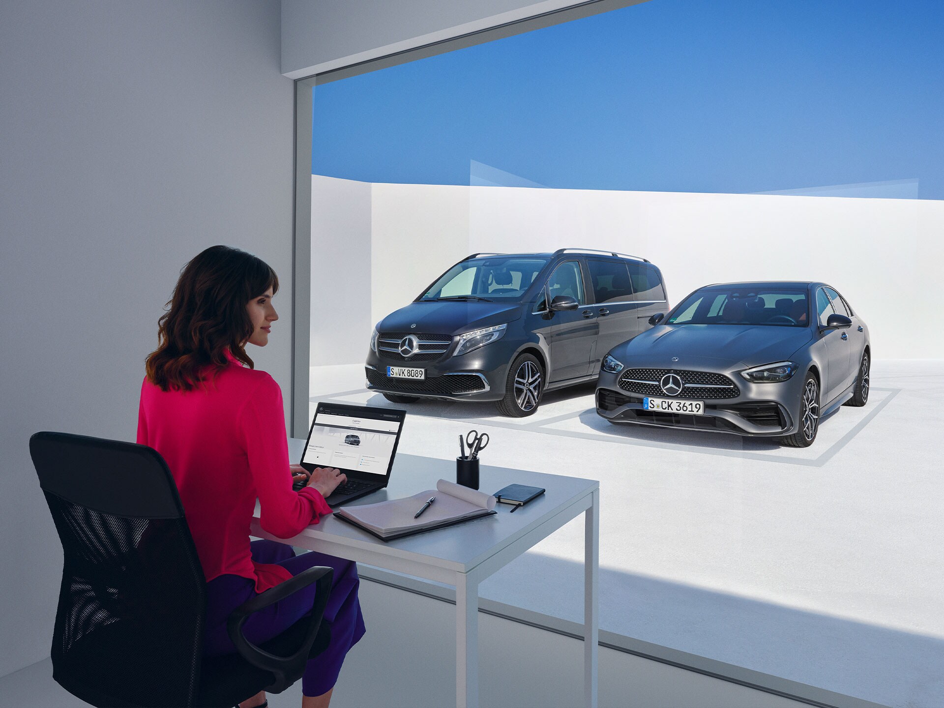 Kvinde sidder ved skrivebord med udkig til en van og personbil fra Mercedes-Benz.