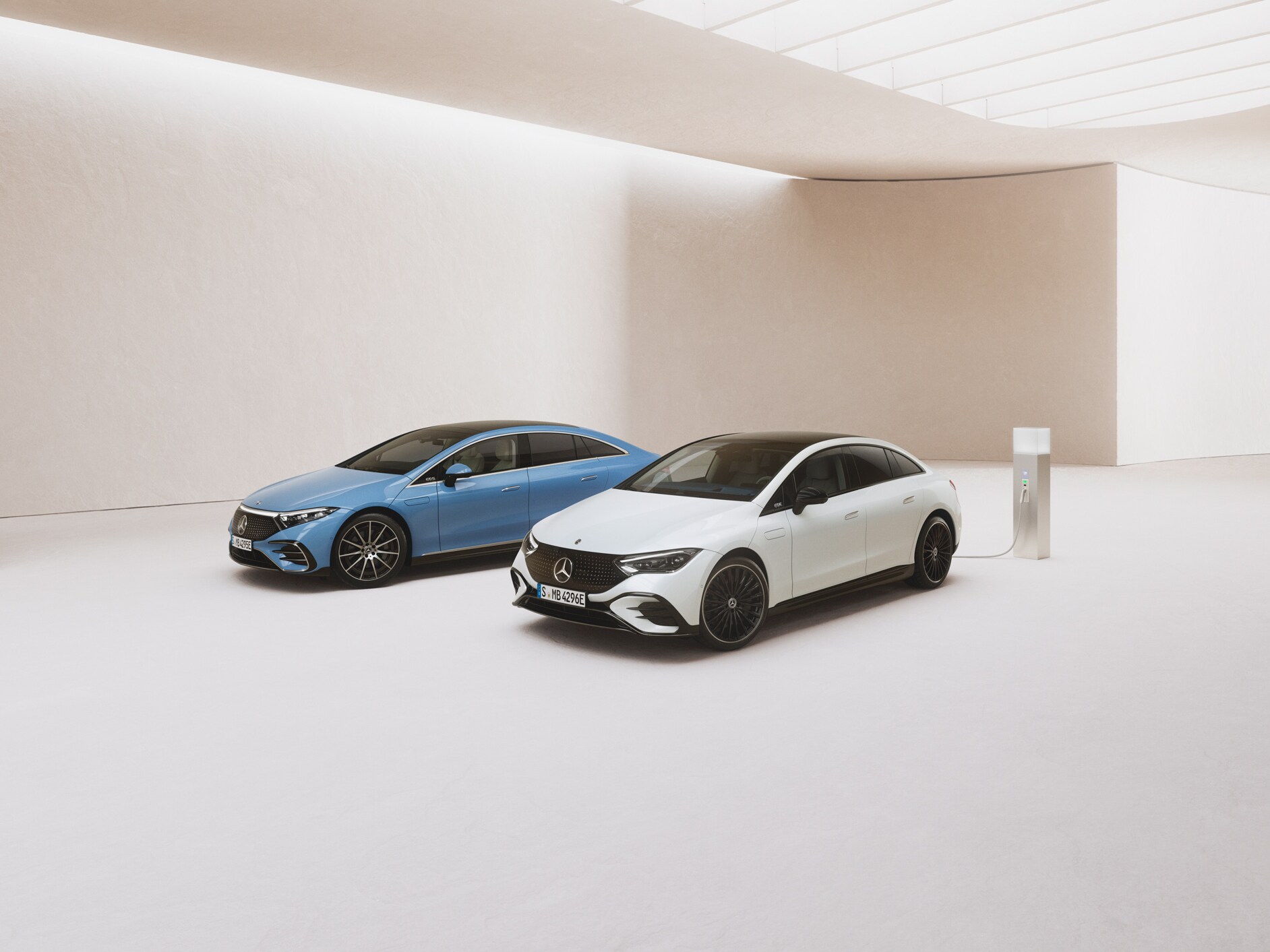 To elektriske Mercedes-Benz biler ved siden af en ladestander i et showroom.