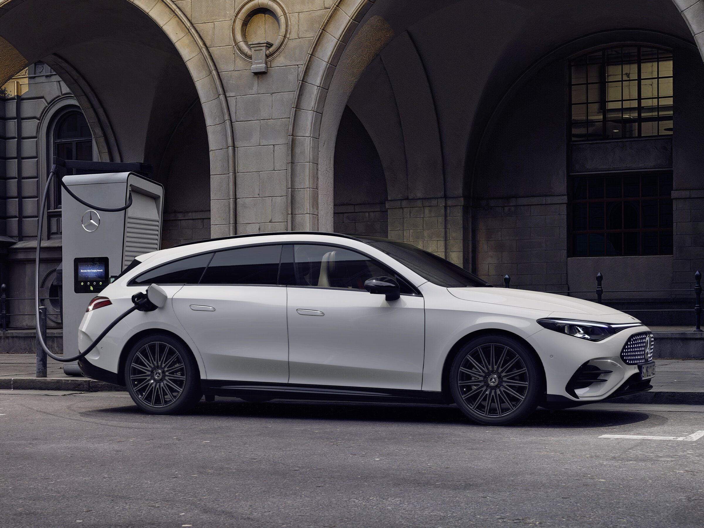 Hvid Mercedes-Benz CLA Shooting Brake tilsluttet ladestander i bymiljø