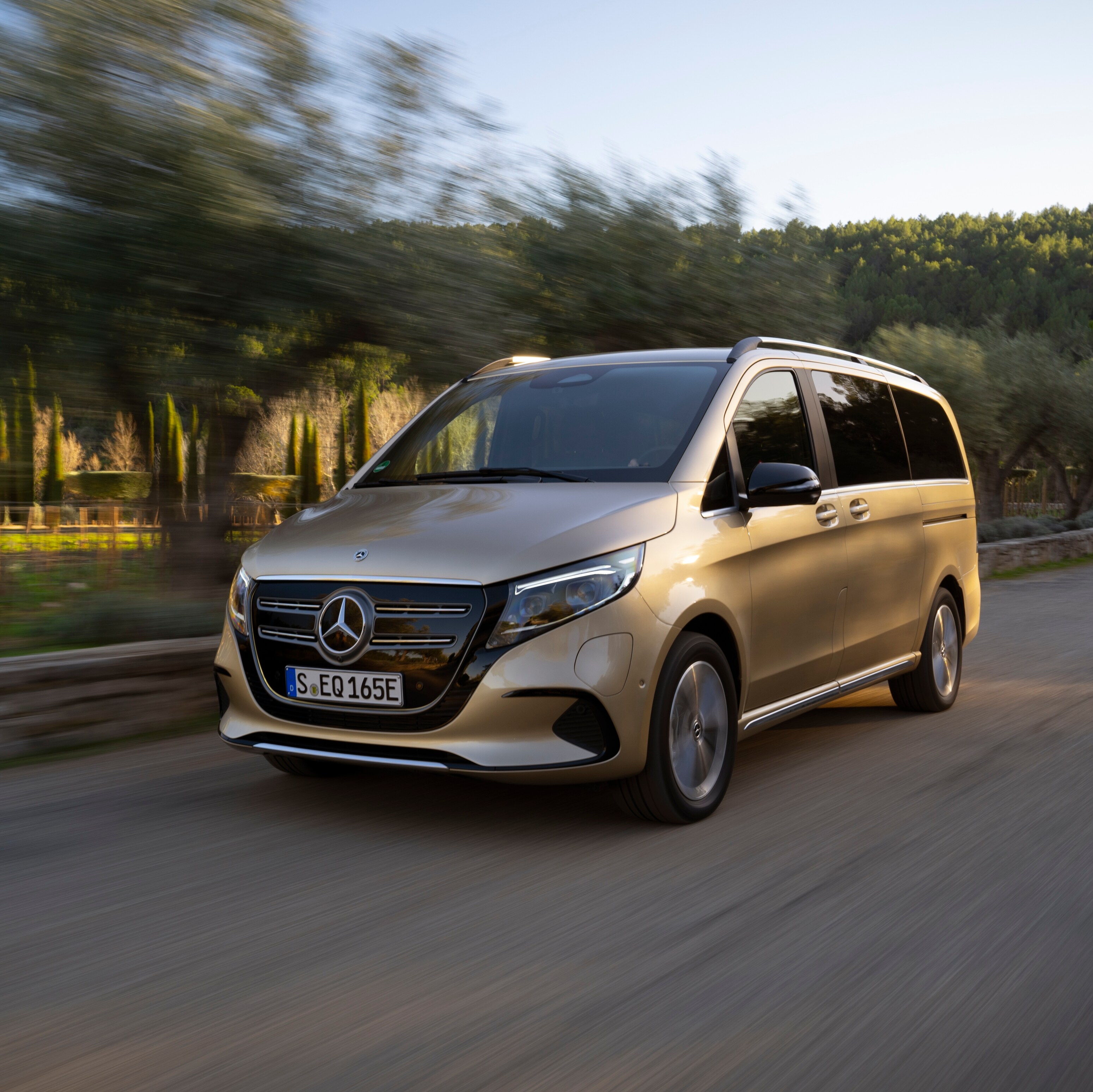 Guldfarvet Mercedes-Benz EQV kører i fuld fart på en vej.