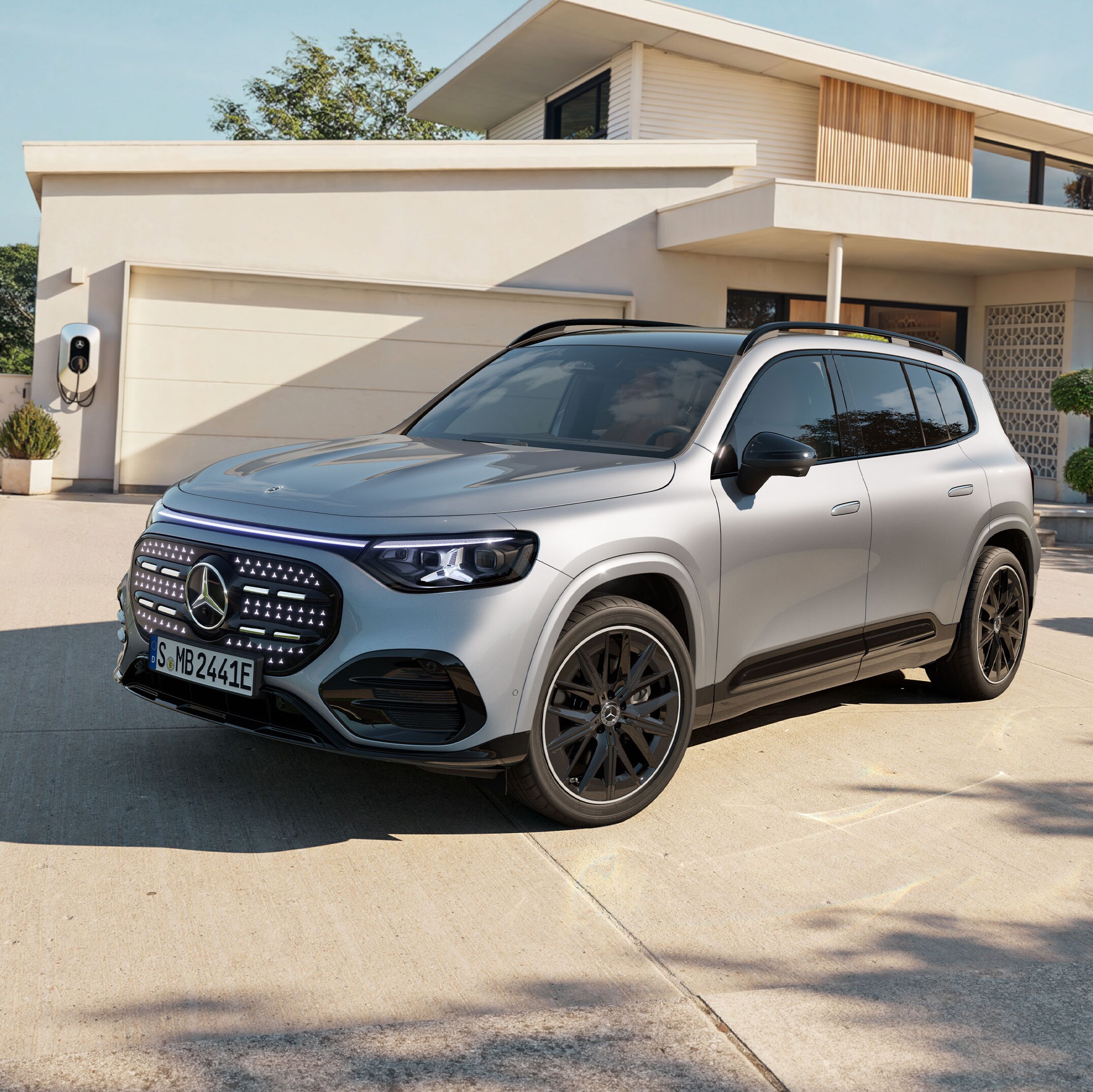 Sølvfarvet Mercedes-Benz GLB with EQ Technology foran hus med garage