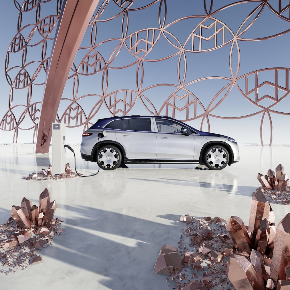 Sidebillede af Mercedes-Maybach EQS SUV ved ladestationen med Maybach-logoet i baggrunden.