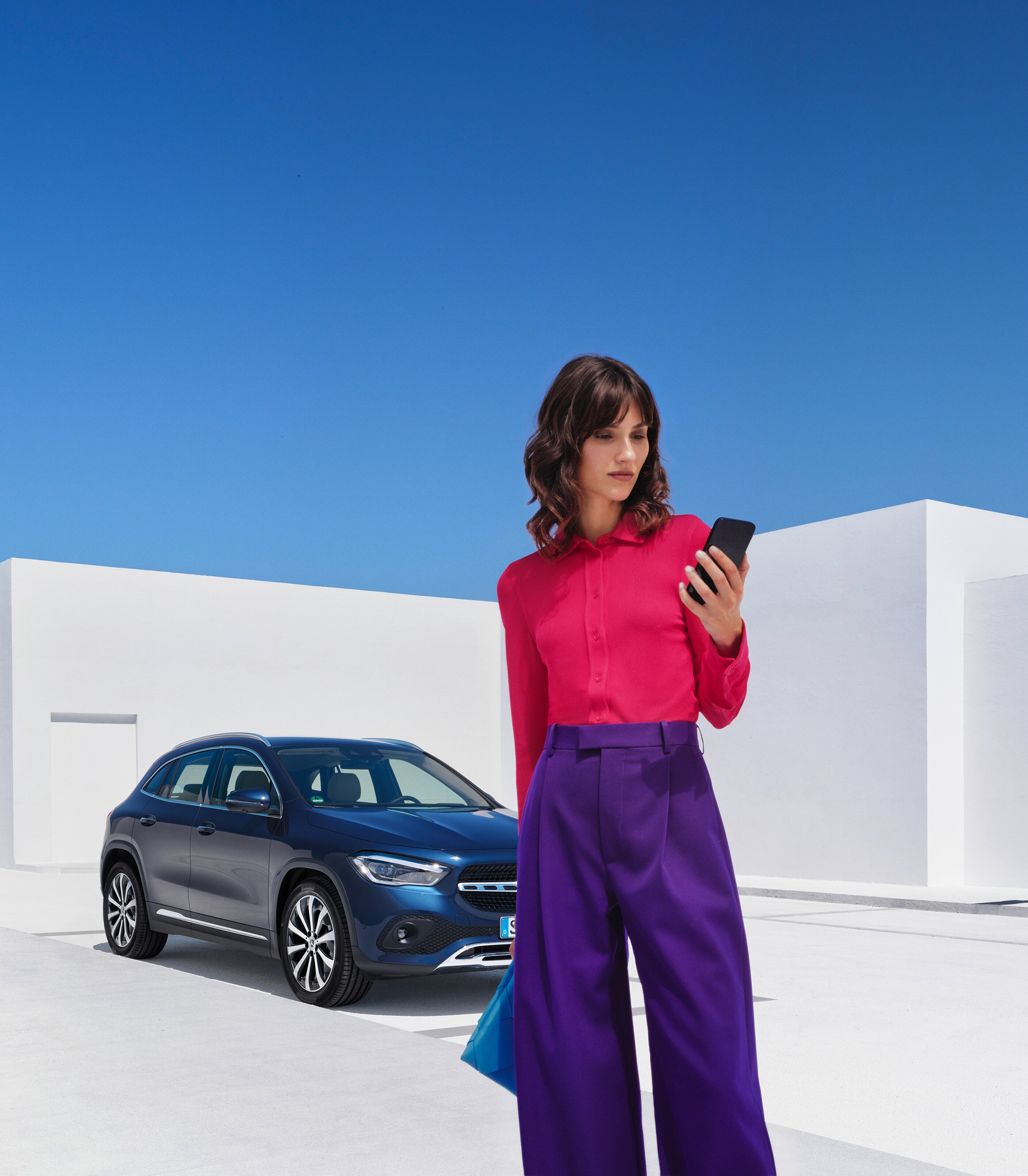 Kvinde står foran sin Mercedes-Benz og kigger på sin smartphone