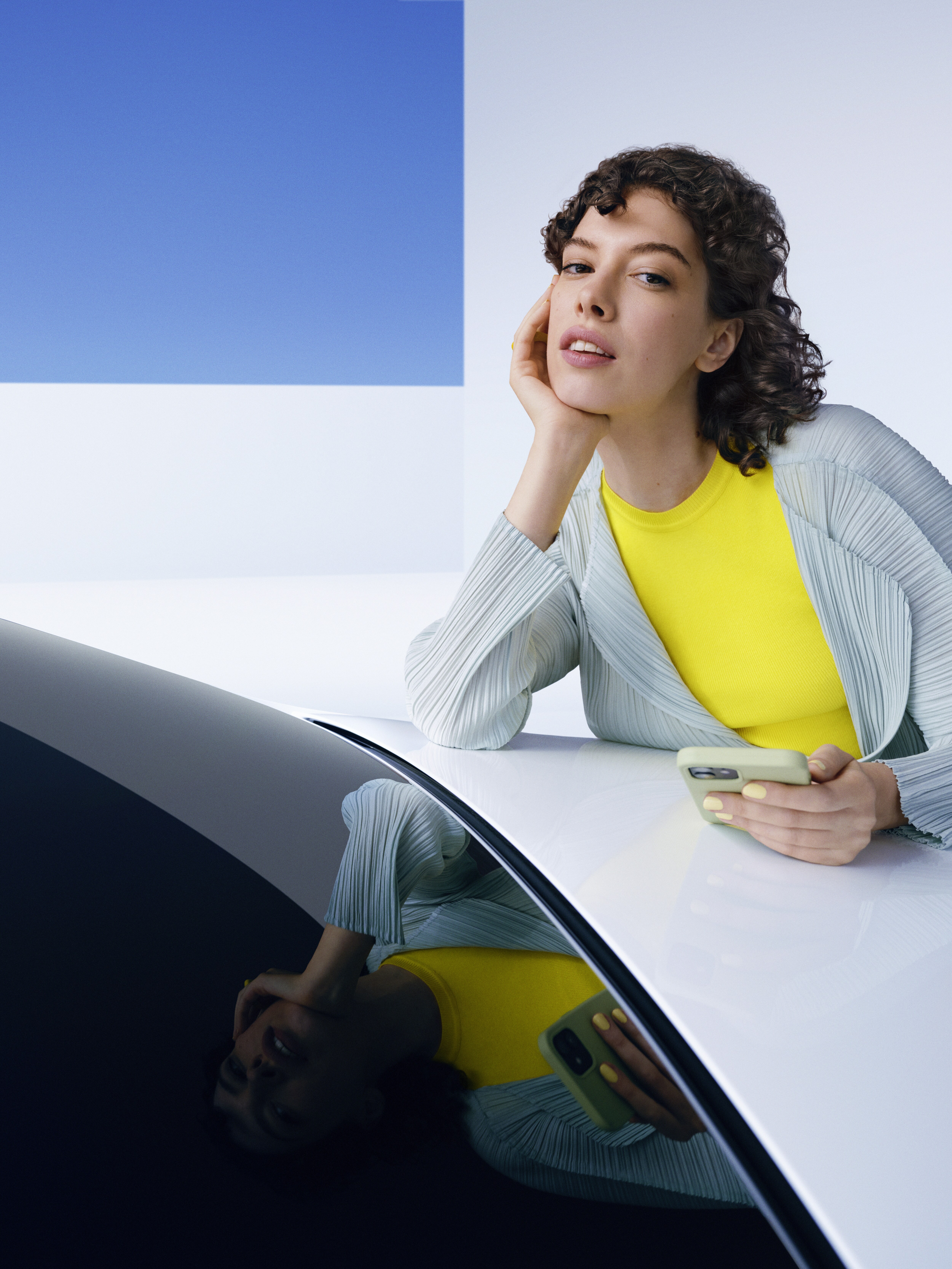 Kvinde læner sig over Mercedes-Benz kølerhjelm med smartphone i hånden