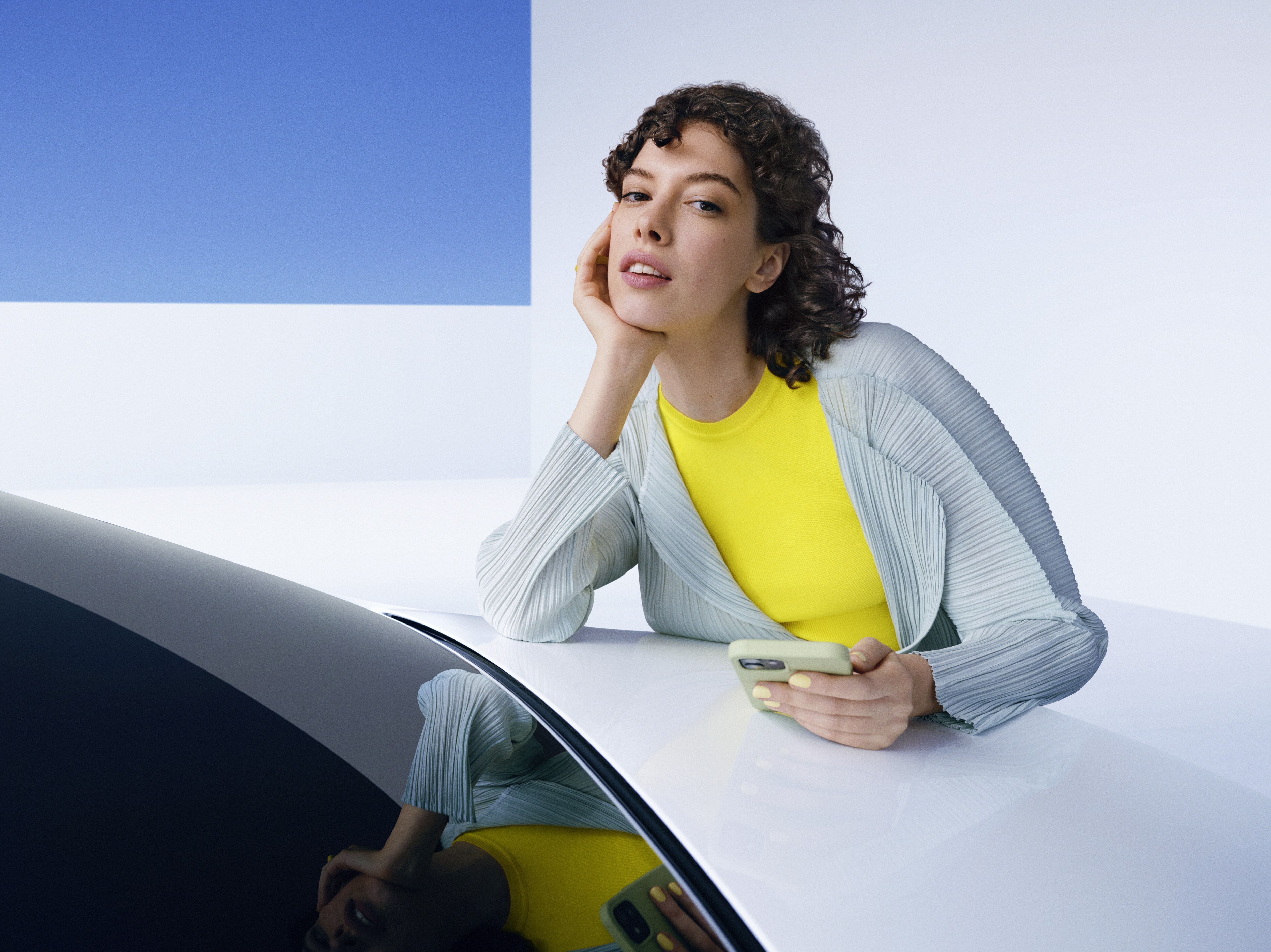 Kvinde læner sig over Mercedes-Benz kølerhjelm med smartphone i hånden