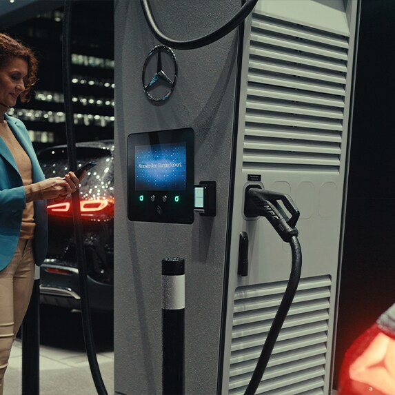 En kvinde med en smartphone i hånden, der står ved siden af en ladestation.