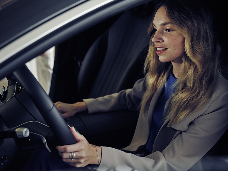 Kvinde sidder i Mercedes-Benz med den ene hånd på rattet