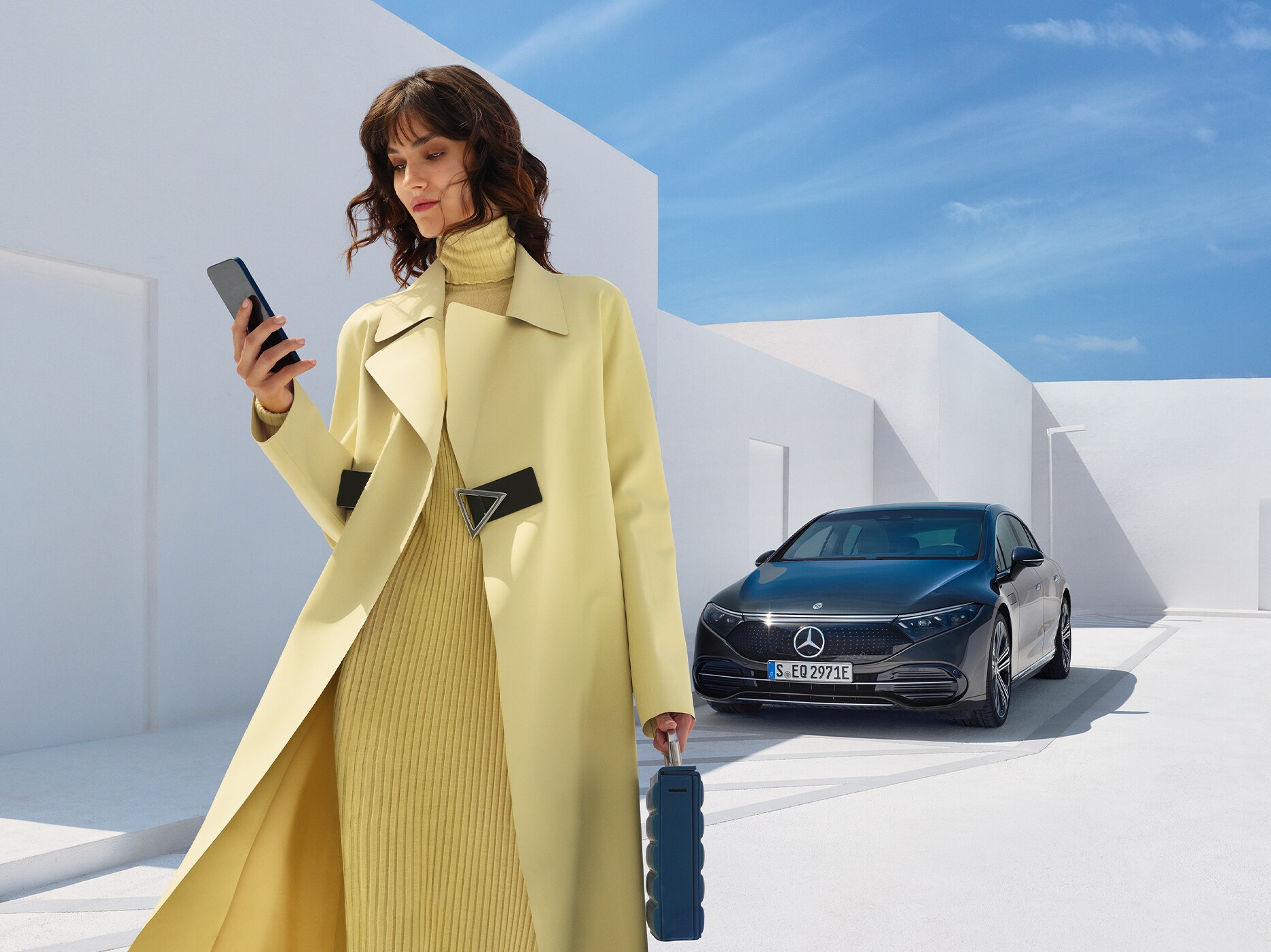 Kvinde står foran sin parkerede Mercedes-Benz og kigger ned i sin telefon