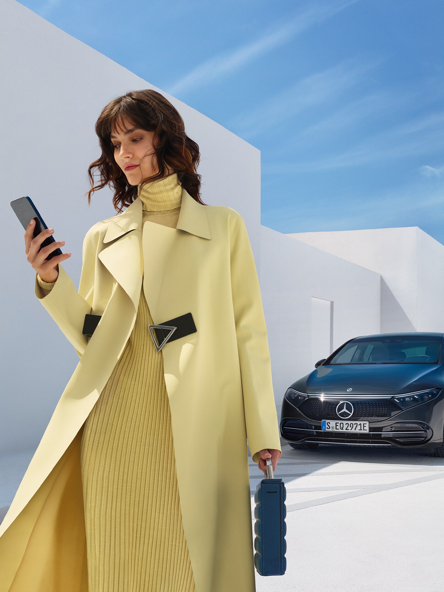 En kvinde står foran en EQS Sedan fra Mercedes-Benz med sin smartphone i hånden