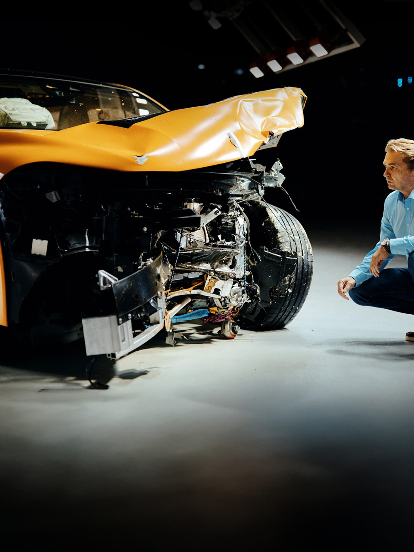 Kollisionstestekspert undersøger en forulykket Mercedes-Benz bil, mens han sidder på hug ved siden af den.