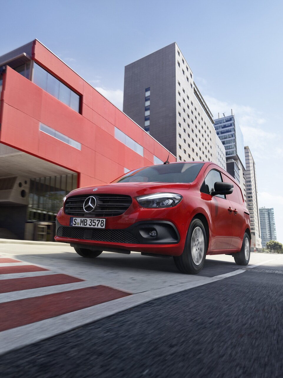 En rød Mercedes-Benz Citan Kassevogn på farten med rød bygning i baggrunden