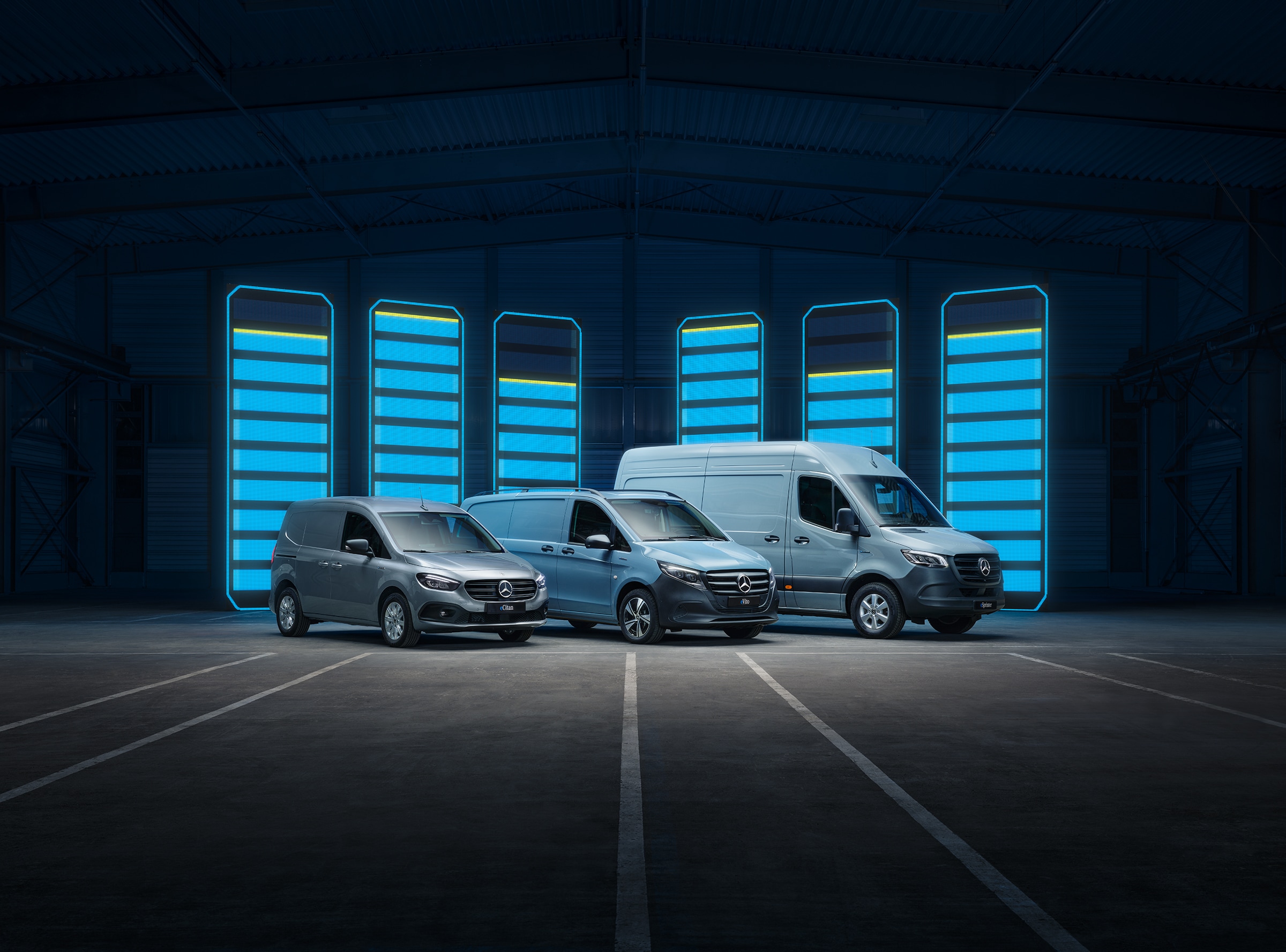 Elektriske varebiler | Historien bag erhvervskøretøjerne | Mercedes-Benz En række Mercedes-Benz elektriske varebiler udstillet i en futuristisk lagerhal