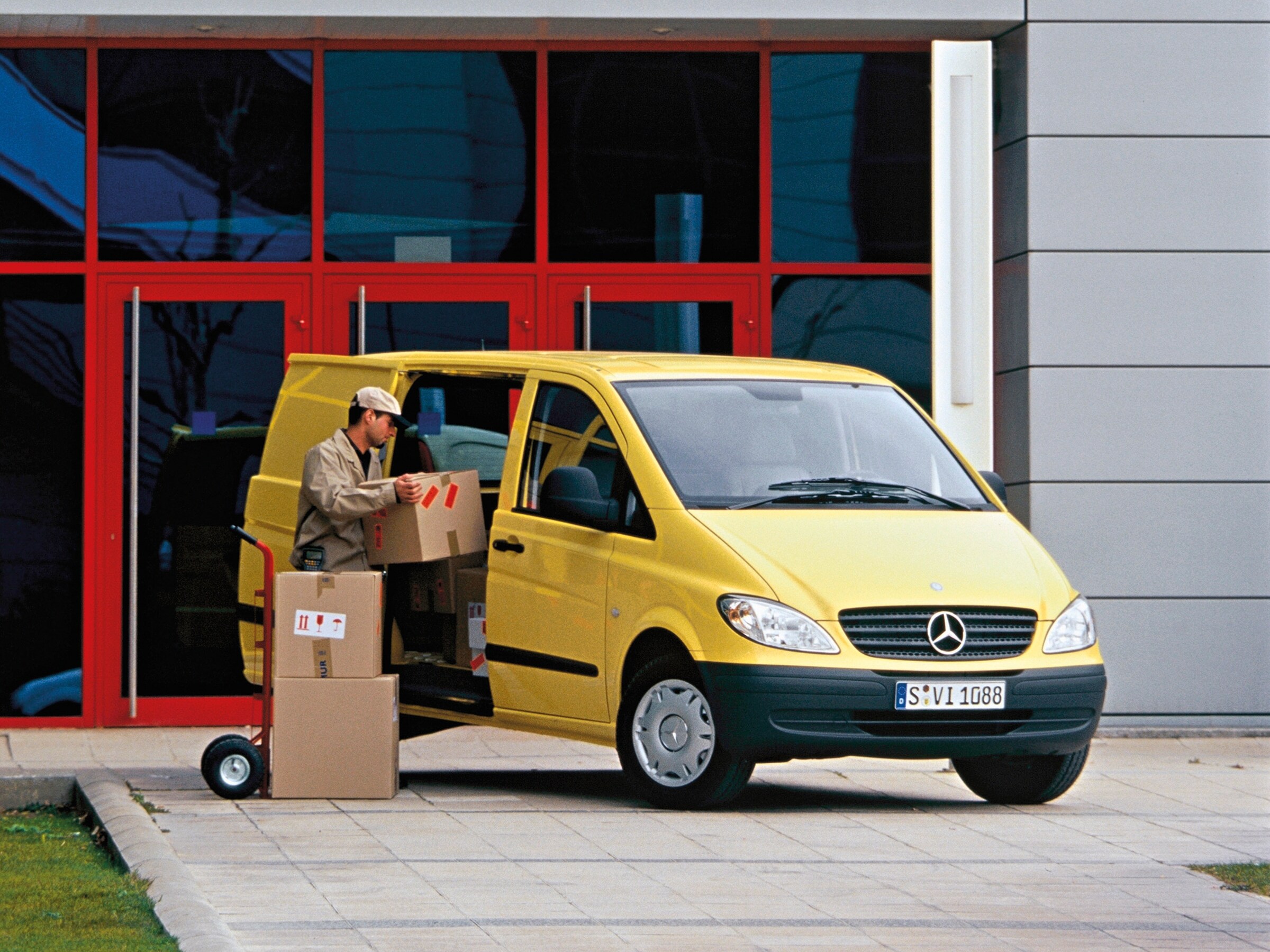 Gul Mercedes-Benz Vito parkeret uden for bygning og en medarbejder læsser pakker
