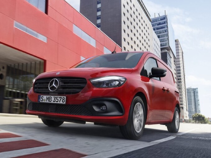 En rød Mercedes-Benz Citan varevogn kører gennem en storby.