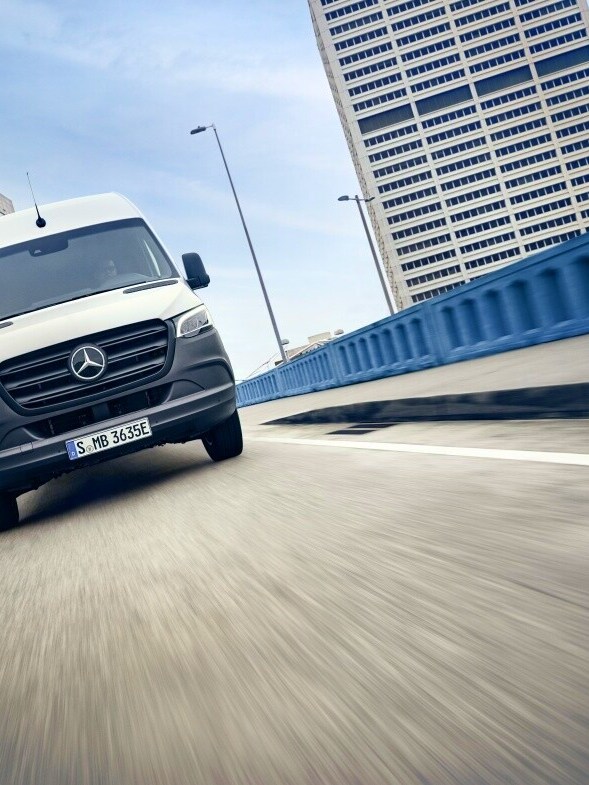 Hvid Mercedes-Benz eSprinter Kassevogn på betonbro med højhuse i baggrunden