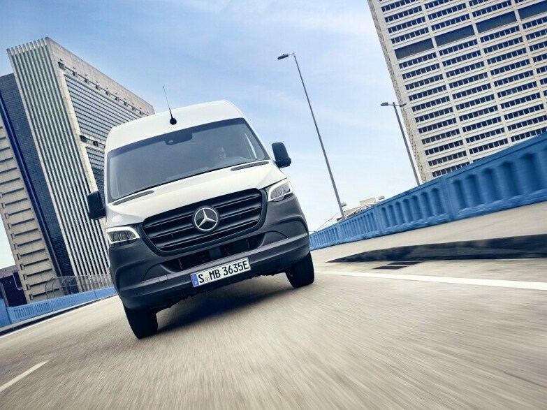 Hvid Mercedes-Benz eSprinter Kassevogn på betonbro med højhuse i baggrunden