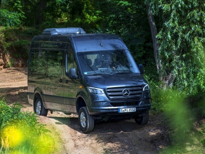 Metallic grå Sprinter Tourer kører på grusvej i løvskov