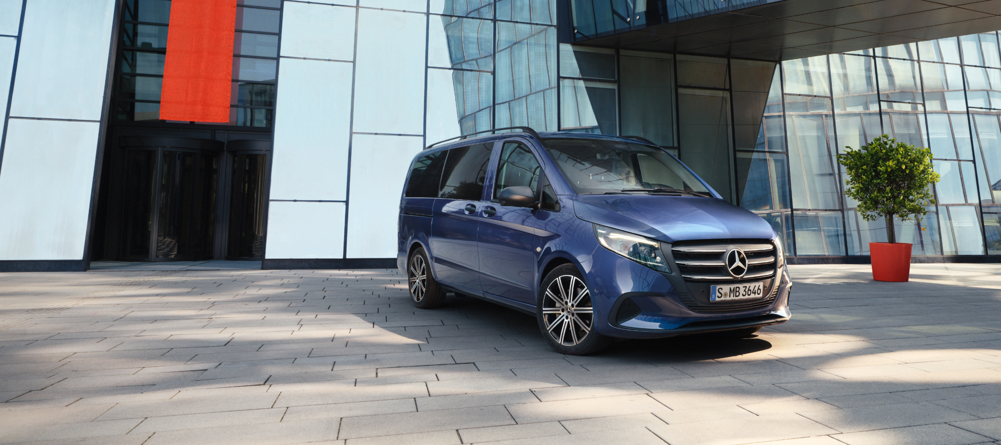 Bilsammenligning | Vito Tourer | Mercedes-Benz Vans Mørk blå Mercedes-Benz Vito Tourer parkeret foran indgang til kontorbygning