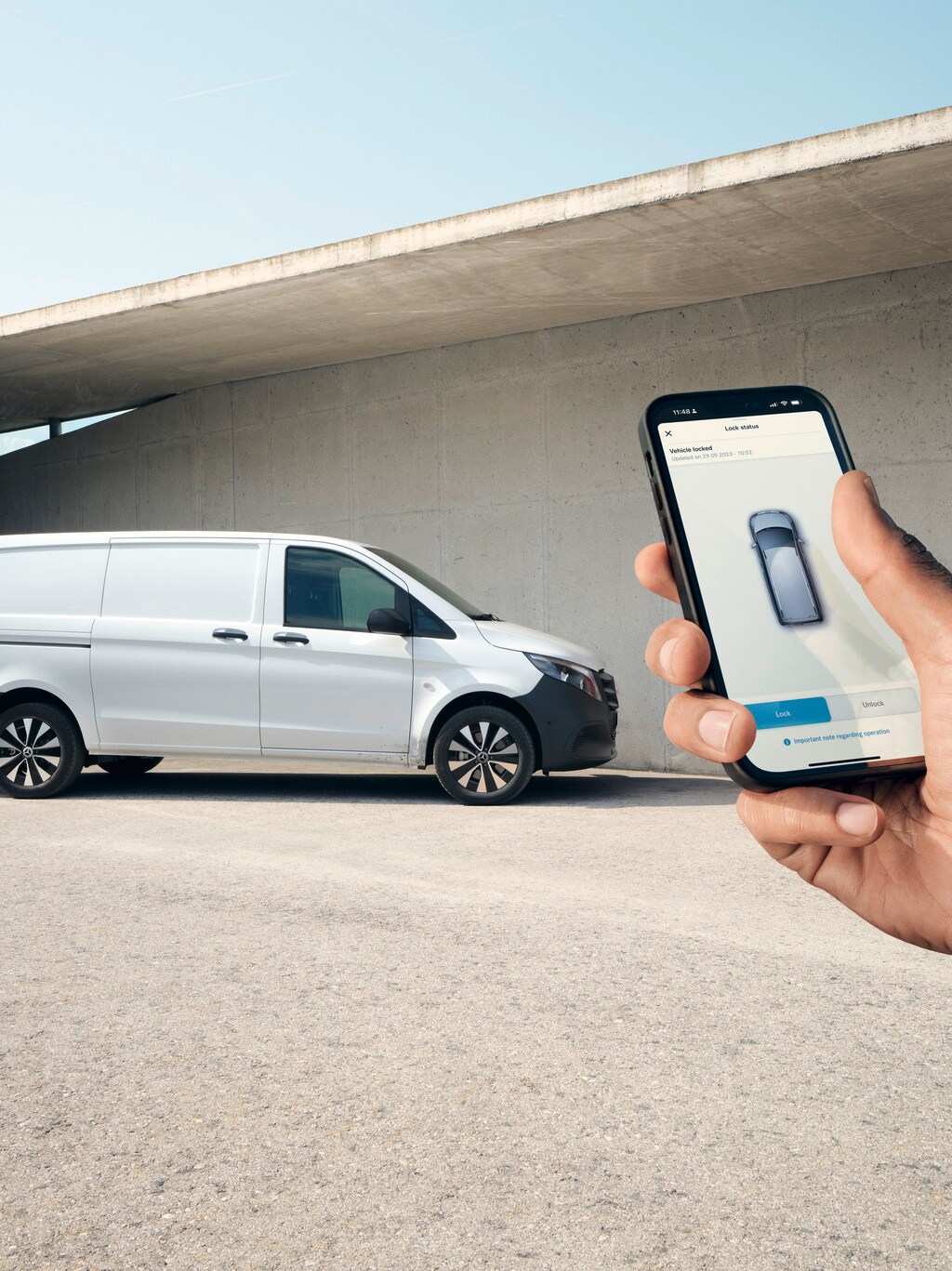 En hånd med en smartphone, der viser Mercedes-Benz appen, med en Vito Kassevogn i baggrunden