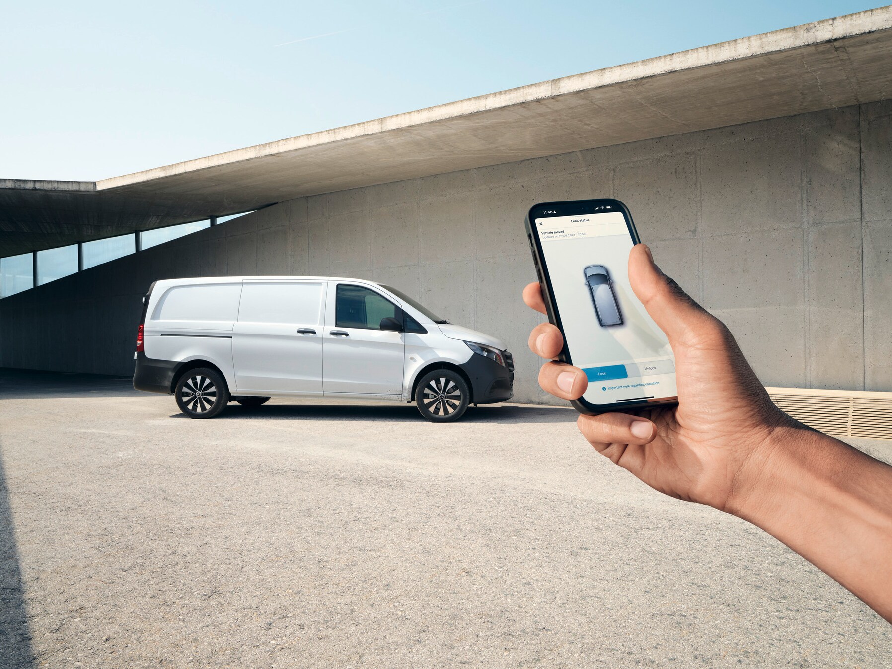 En hånd holder en smartphone, der viser Mercedes me appen. En Vito kassevogn er i baggrunden.