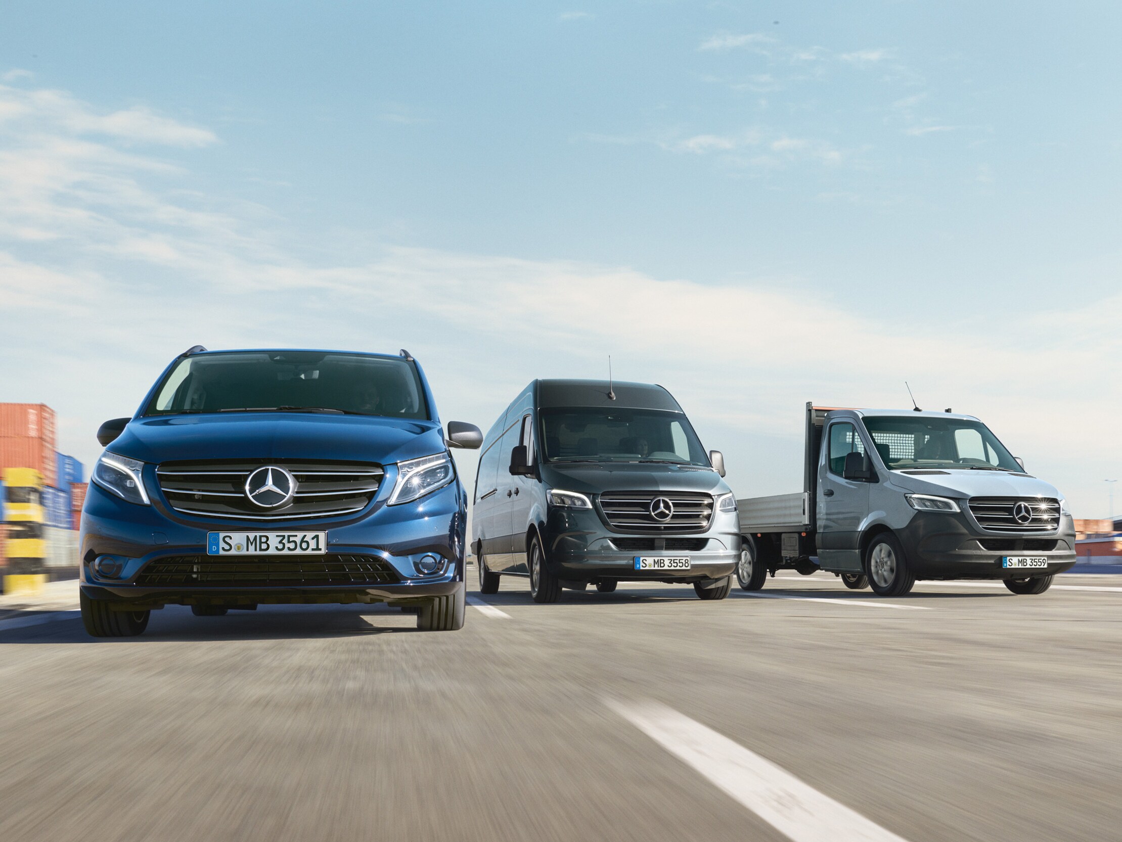 En række Mercedes-Benz varebiler parkeret side om side på en vej ved siden af en læsserampe.