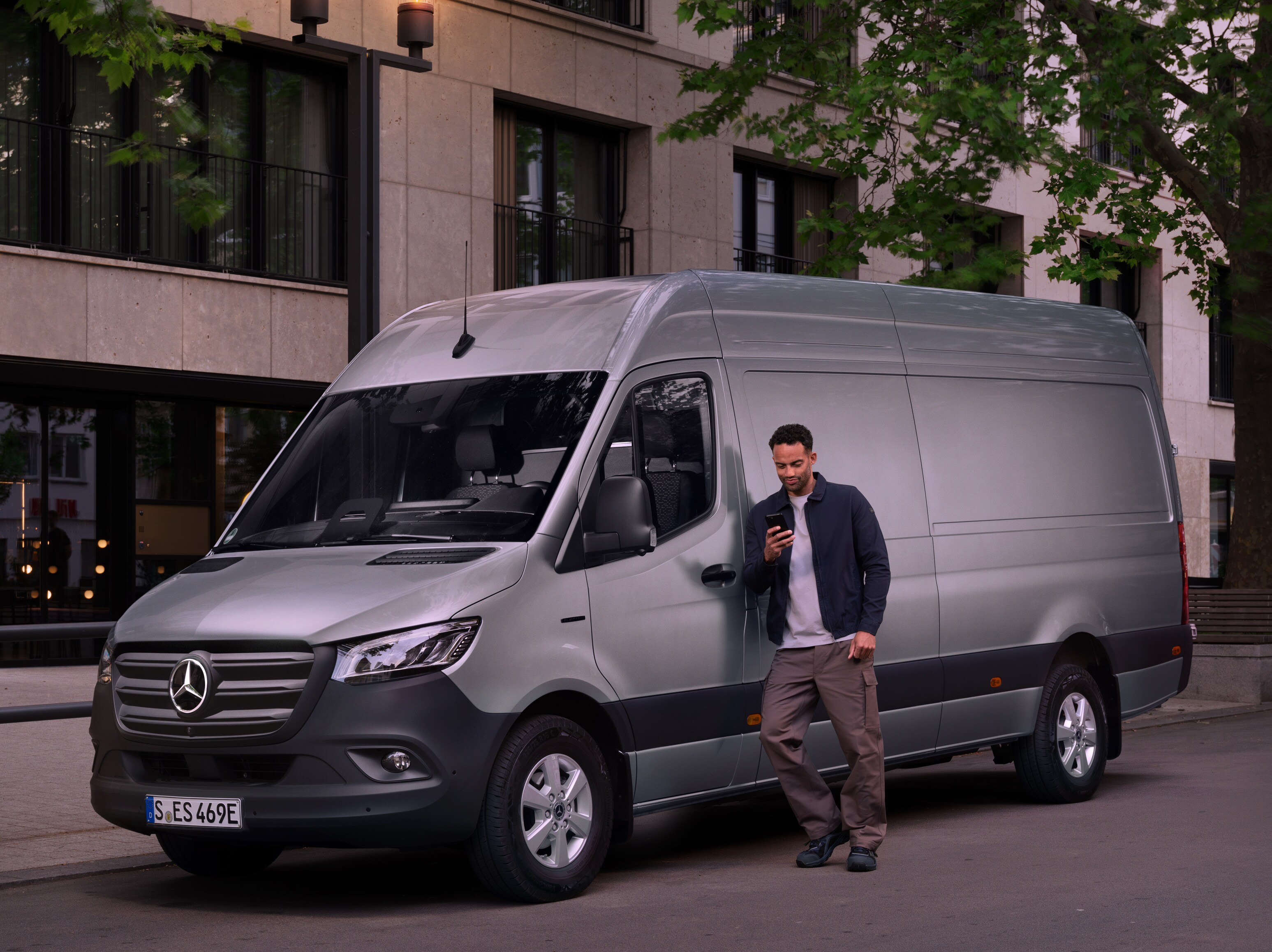 Mand læner sig op ad en sølvfarvet Mercedes-Benz Sprinter varebil.