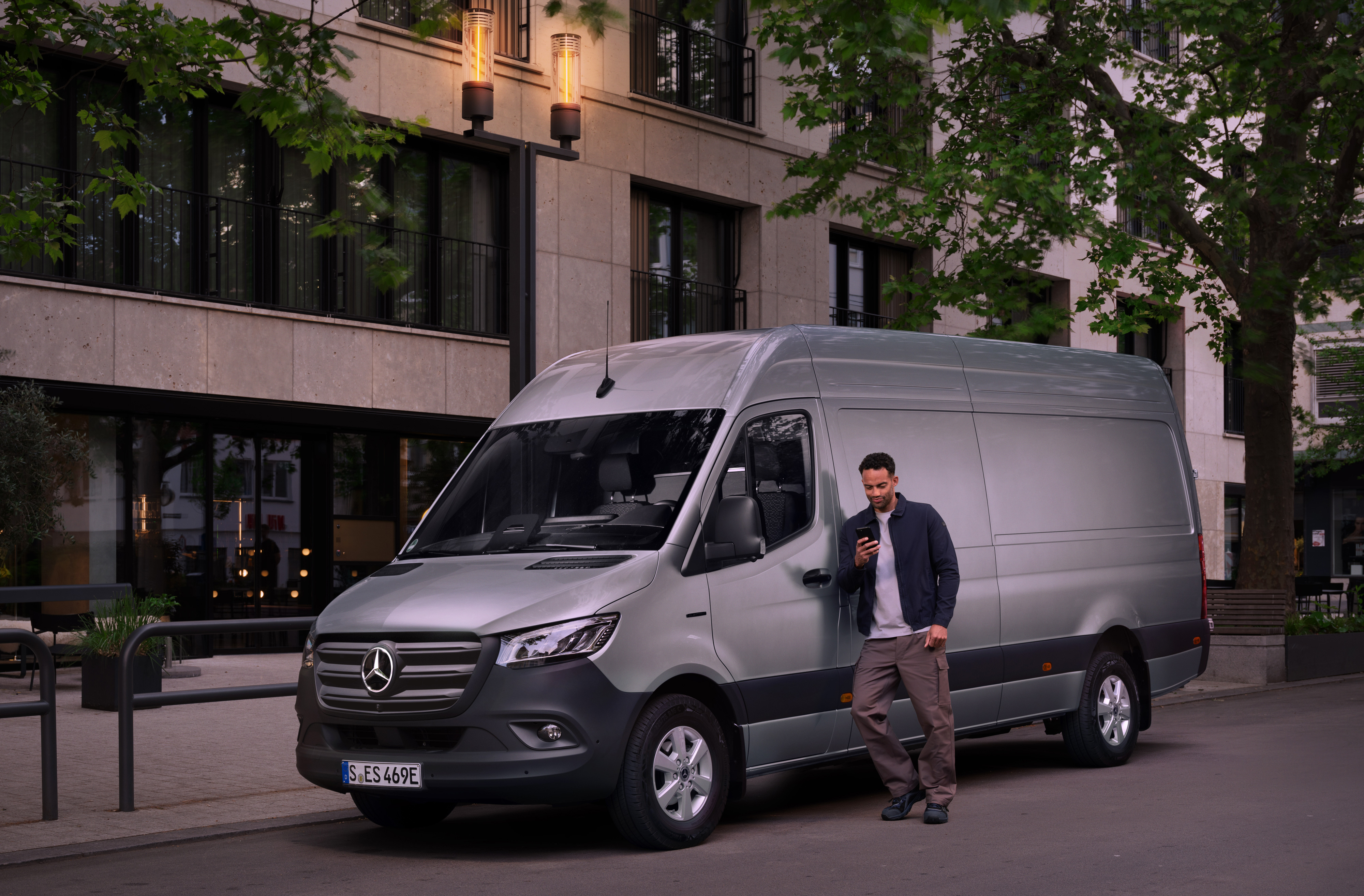 Mercedes-Benz | Varebilsservice | Customer Assistance Center Mand læner sig op ad en sølvfarvet Mercedes-Benz Sprinter varebil.