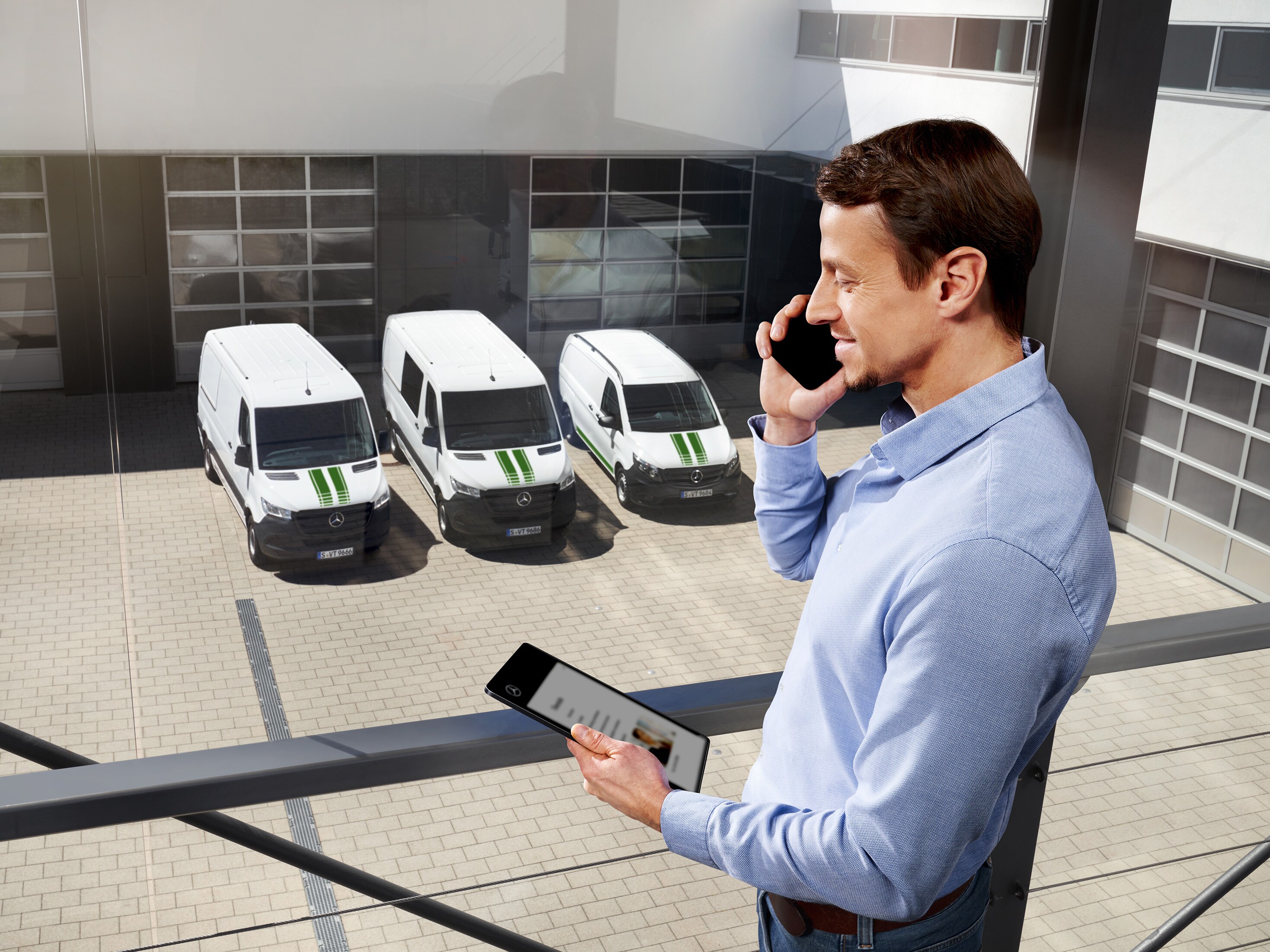 Mand taler i mobiltelefon foran hvide Mercedes-Benz varebiler på en parkeringsplads.