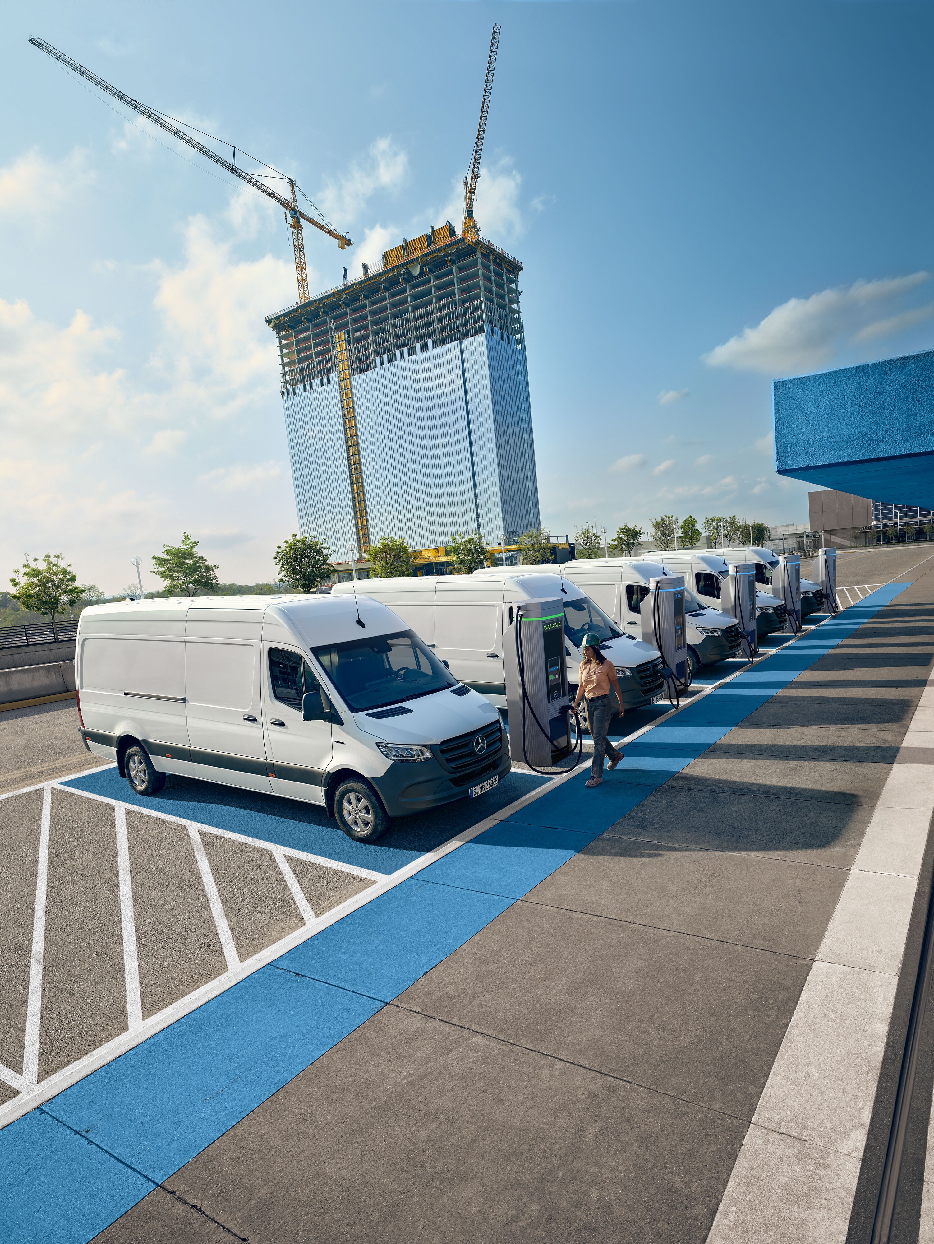 Flere hvide Mercedes-Benz Sprinter varebiler oplader ved ladestationer.