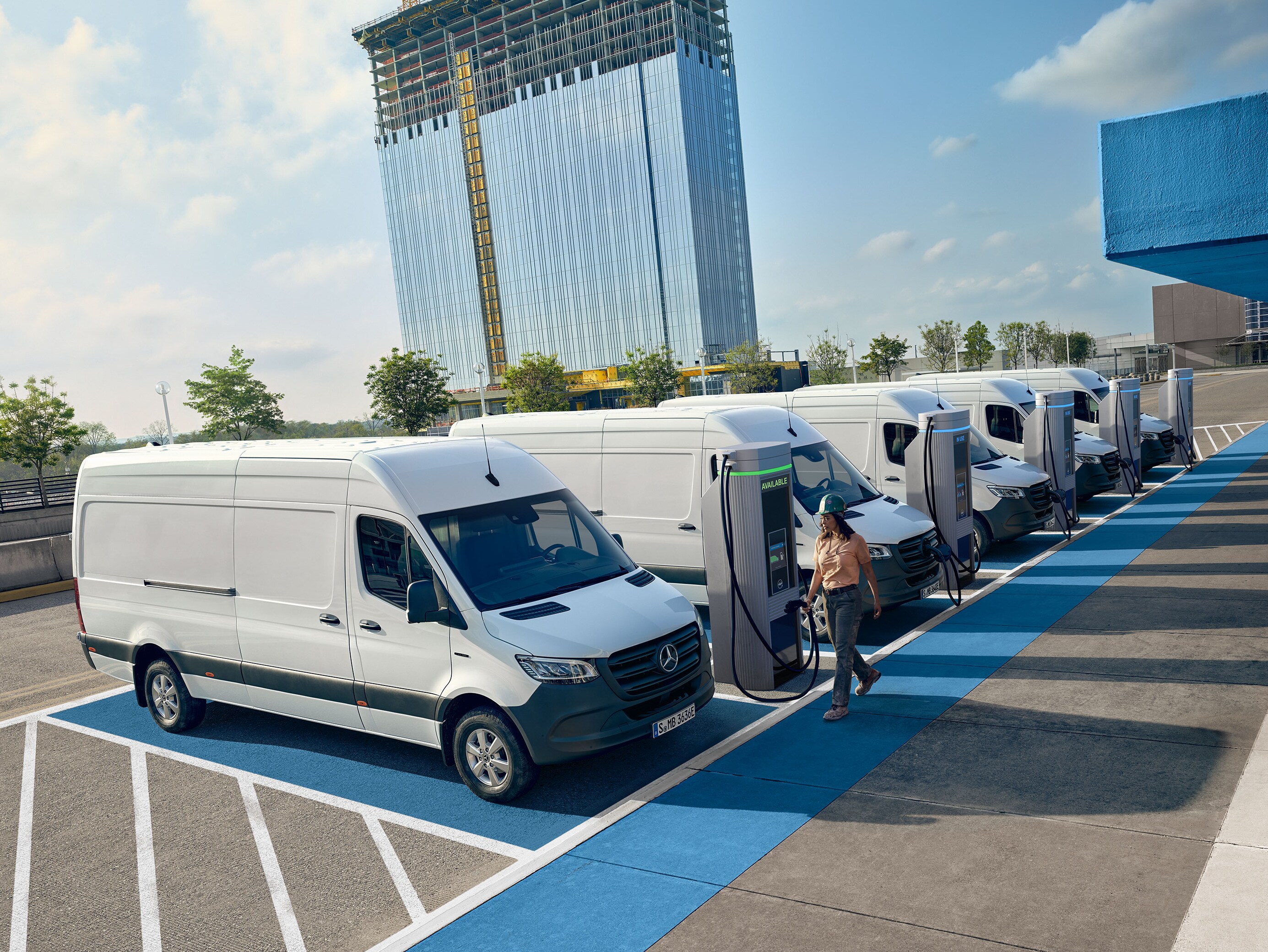 Flere hvide Mercedes-Benz Sprinter varebiler oplader ved ladestationer.