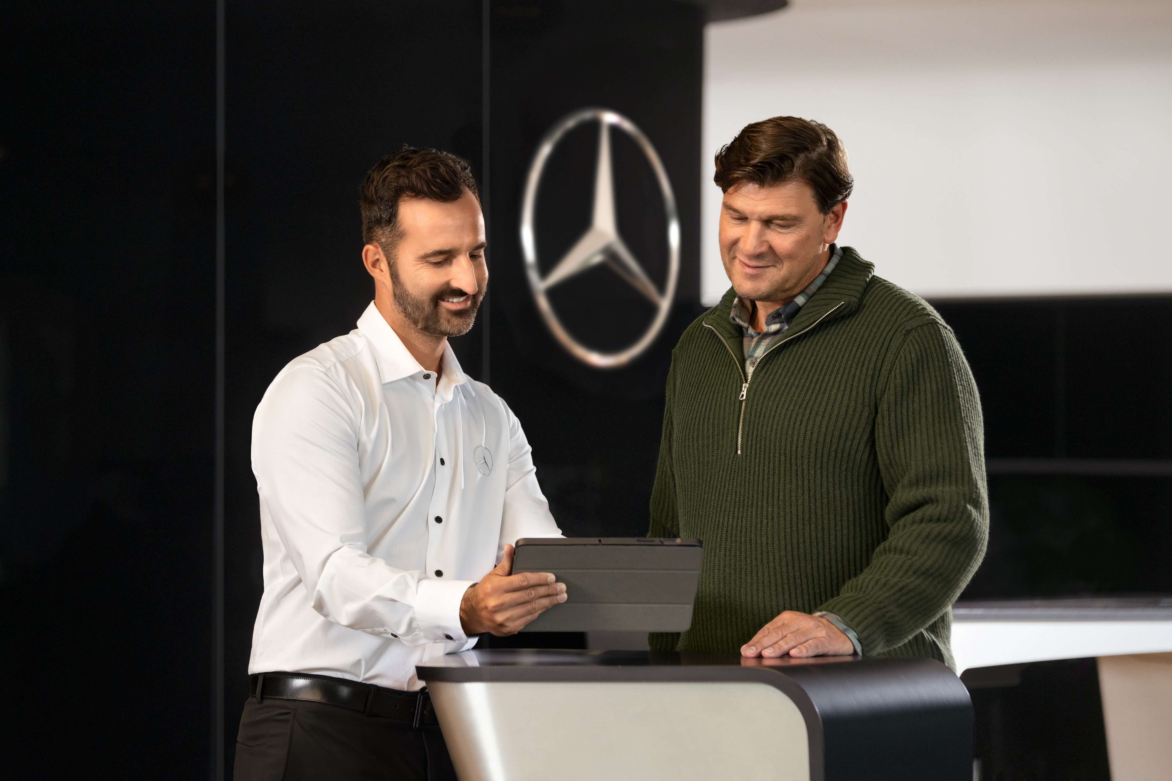 Mercedes-Benz | Mobilitetsløsninger | Serviceværksted Mercedes-Benz medarbejder taler med en kunde og kigger på en tablet.