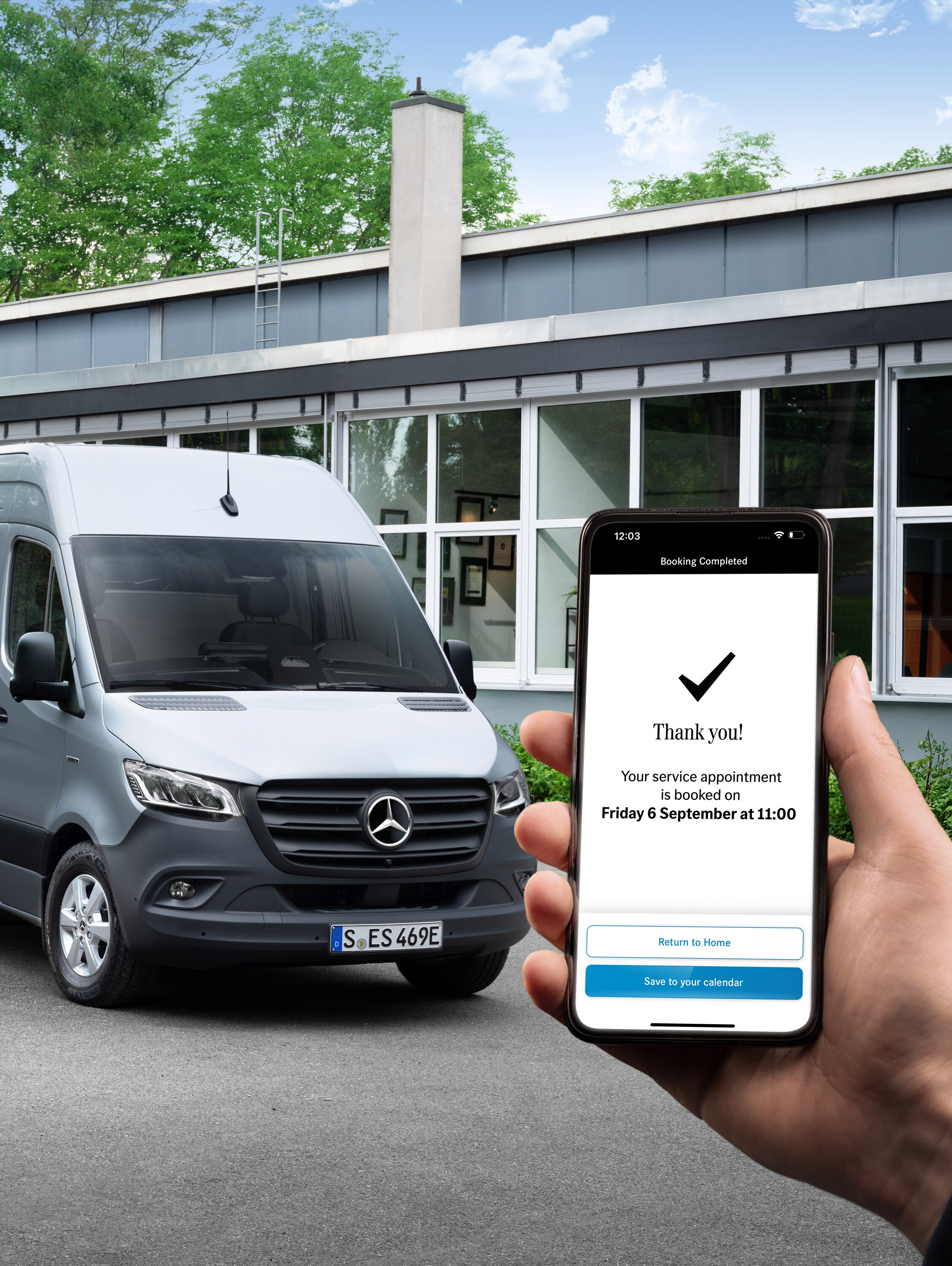 En grå Mercedes-Benz Sprinter varebil foran et kontor med en person, der holder en smartphone i forgrunden.