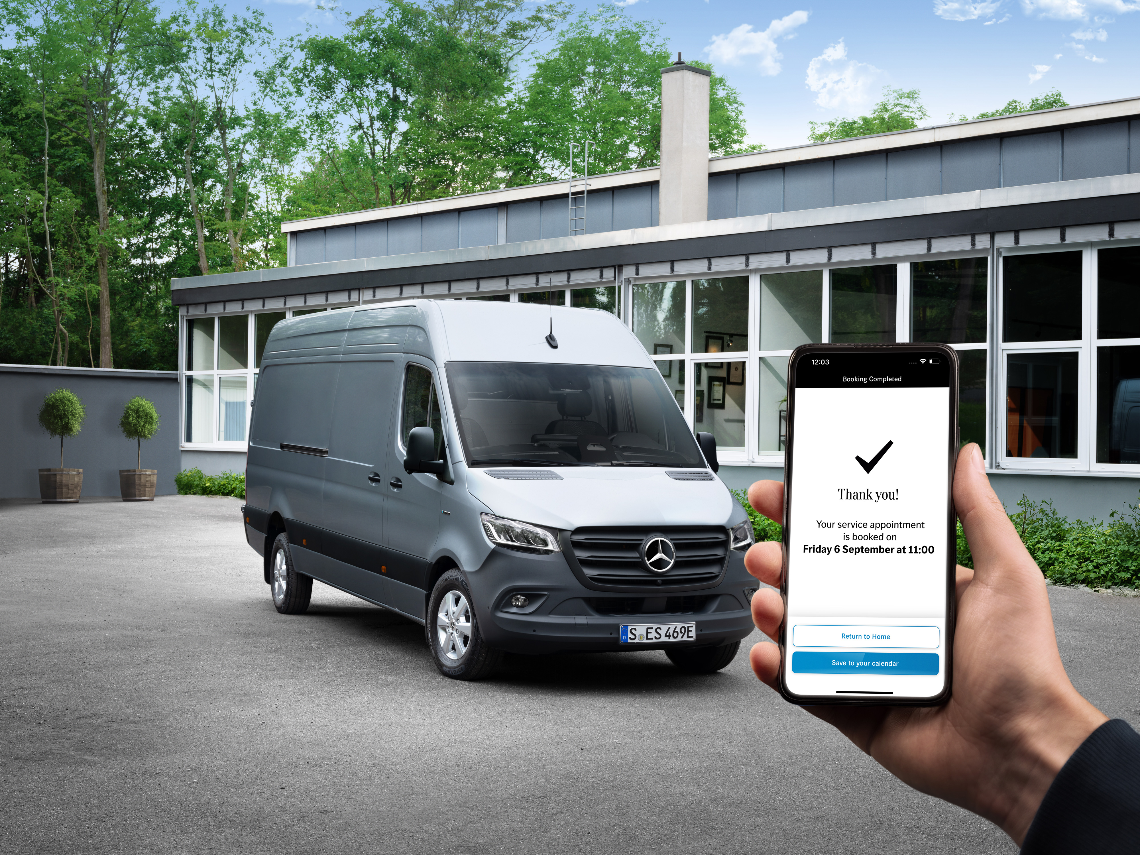 Mercedes-Benz | Bekvemmelighed | Serviceværksted En grå Mercedes-Benz Sprinter varebil foran et kontor med en person, der holder en smartphone i forgrunden.