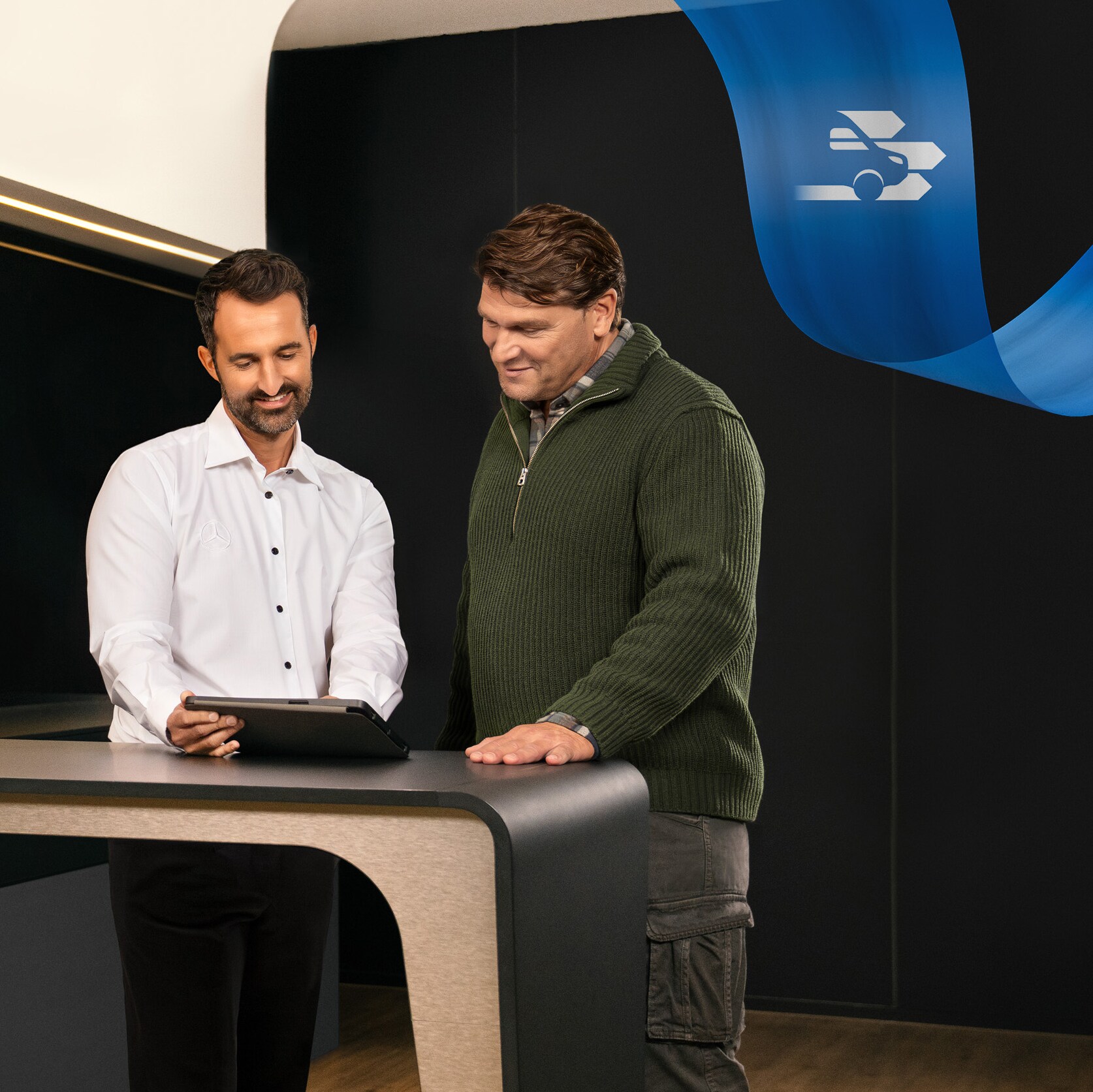 To mænd står på kontoret i et Mercedes-Benz serviceværksted og taler om noget, de har set på en tablet.