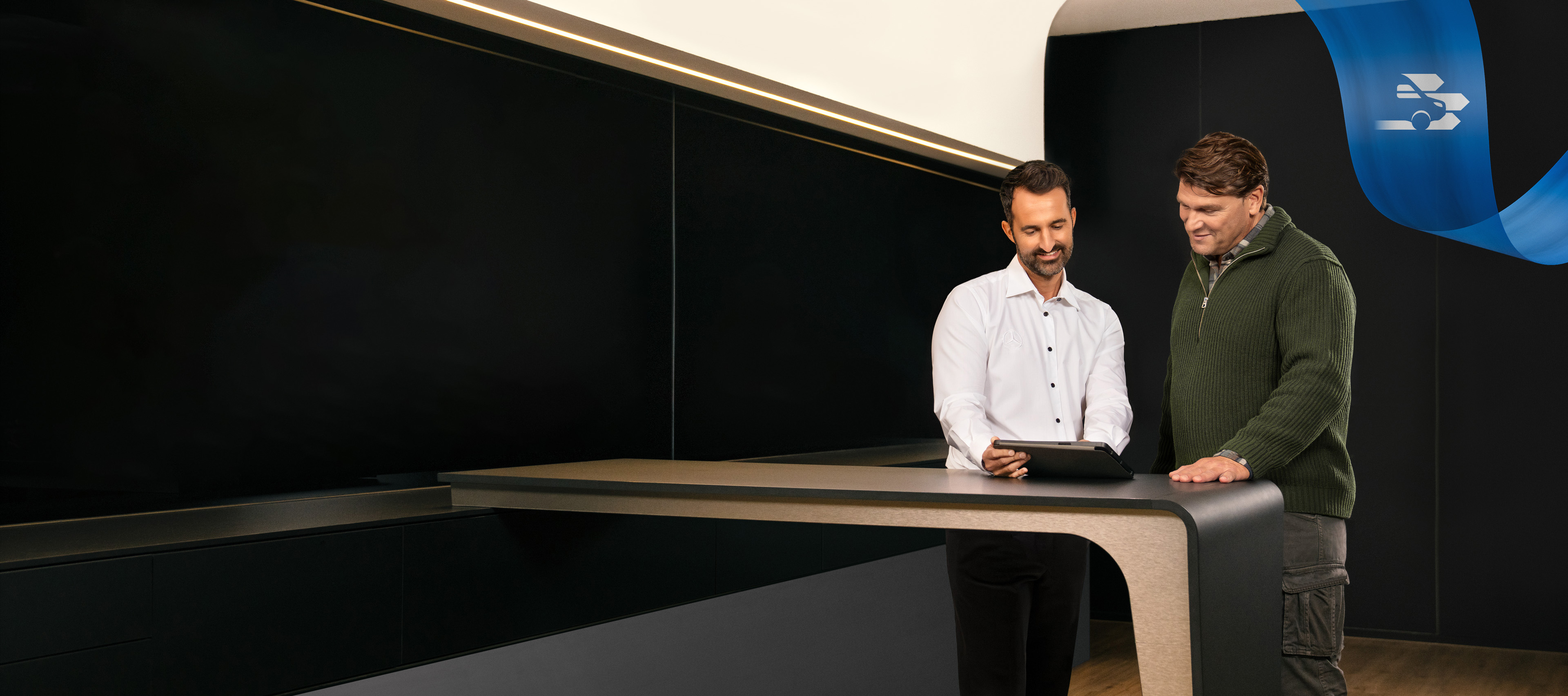 Mercedes-Benz | Bekvemmelighed | Serviceværksted To mænd står på kontoret i et Mercedes-Benz serviceværksted og taler om noget, de har set på en tablet.