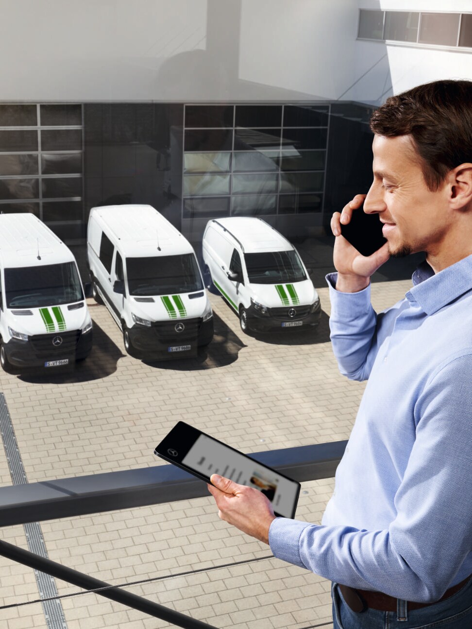 Konsulent med en telefon og en tablet i hånden og Mercedes-Benz varebiler i baggrunden.