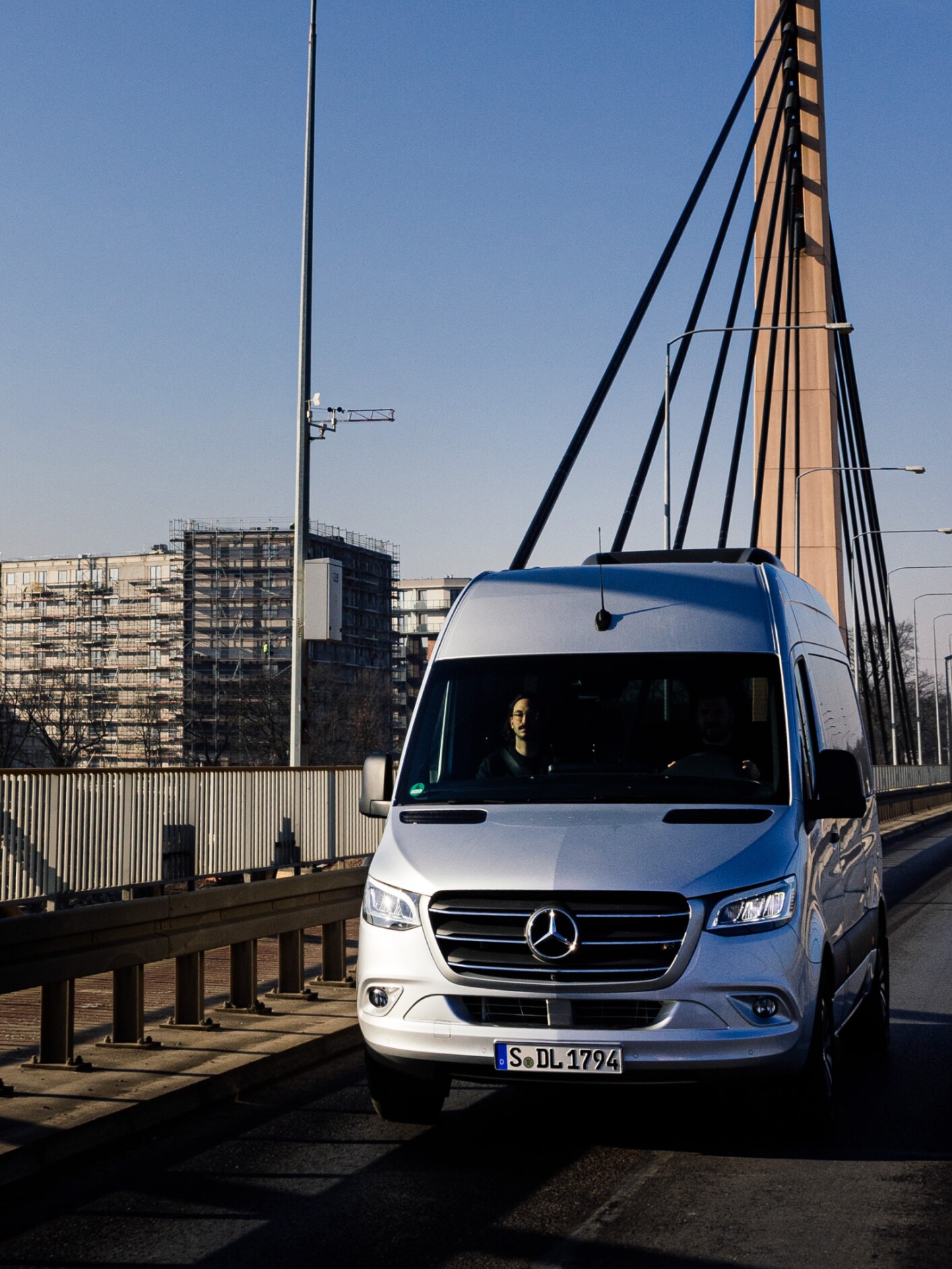 En Mercedes-Benz varebil kører over en bro med bygninger i baggrunden